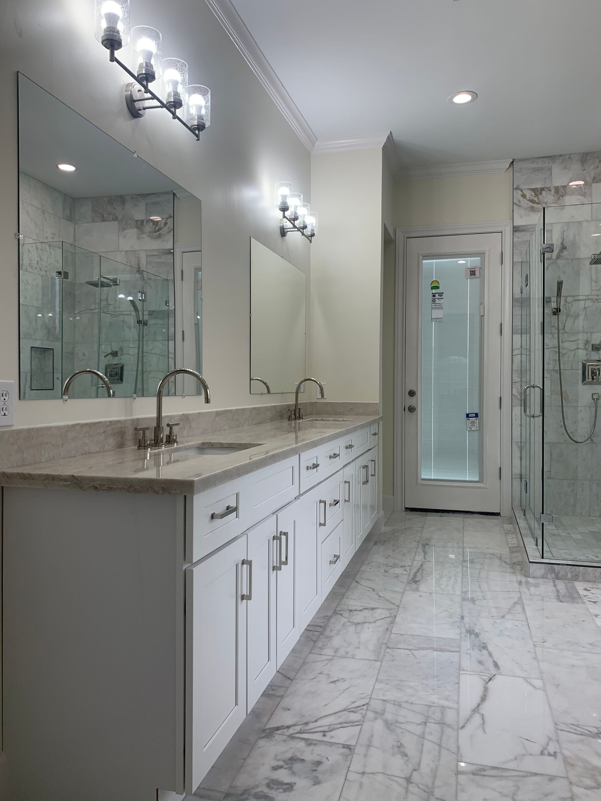 Modern bathroom with double vanity, marble floor, glass shower, and large mirror.