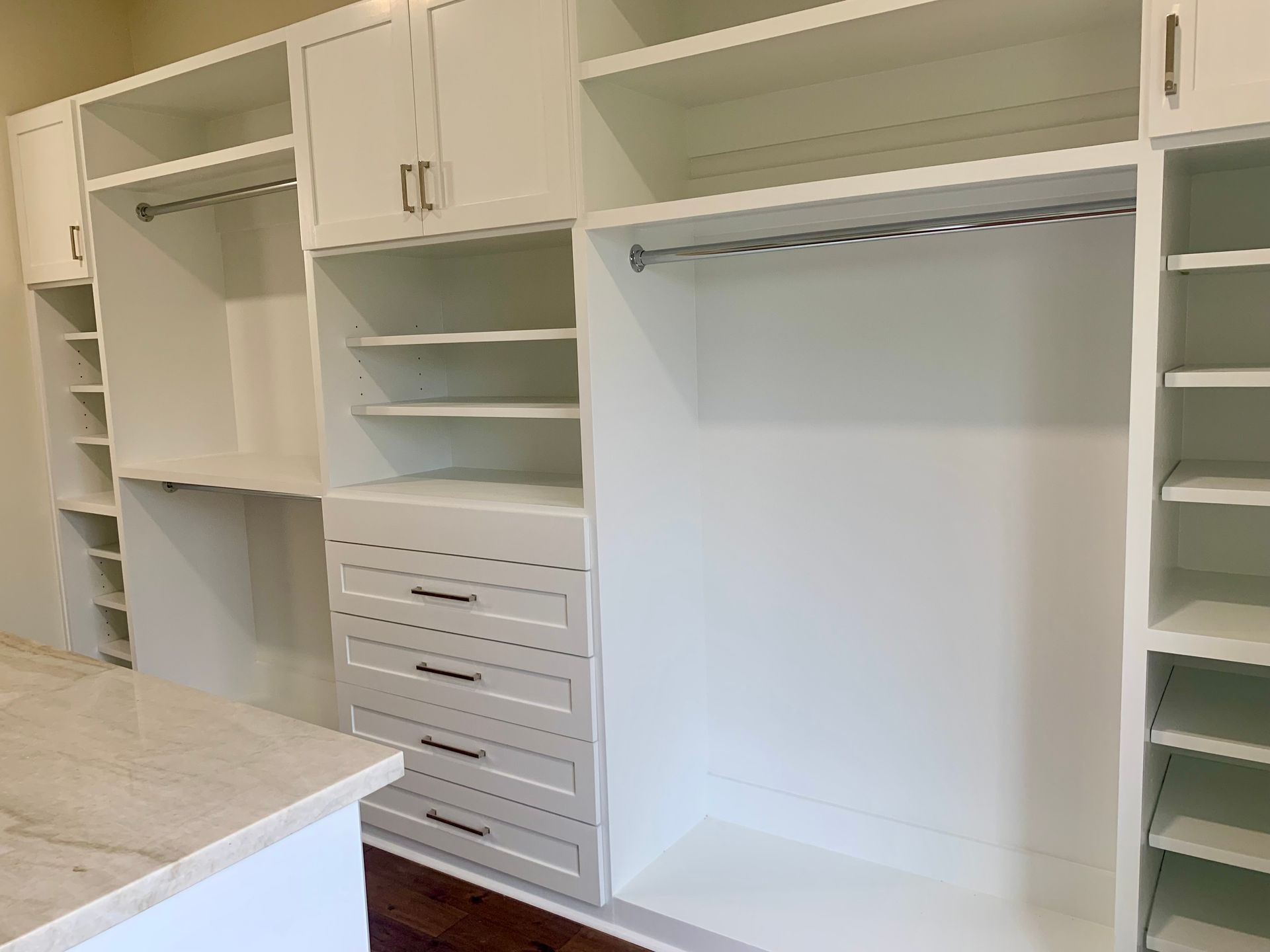 Built-in white closet shelving and drawers in a walk-in closet with a marble countertop at left
