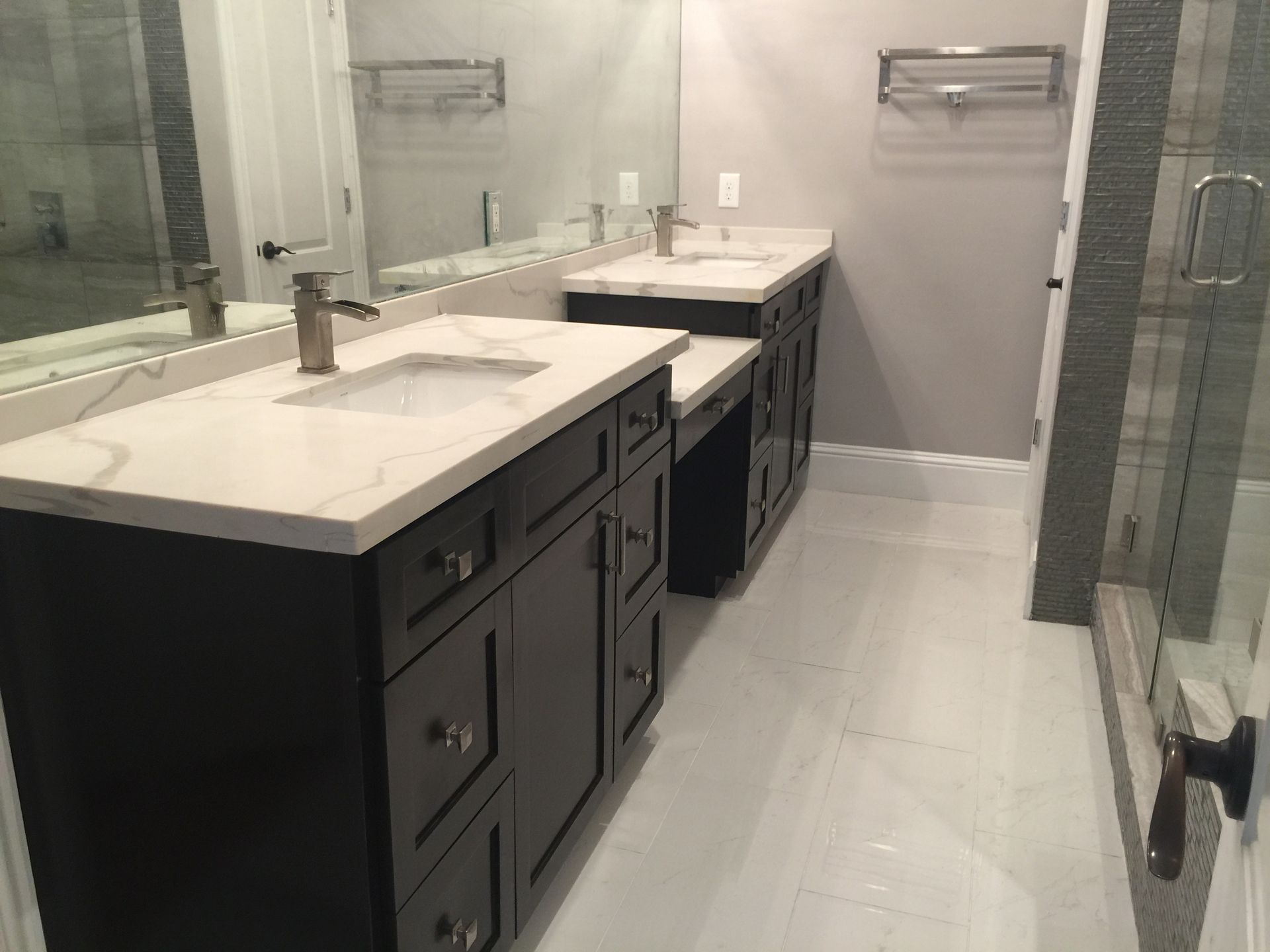 Modern bathroom with double vanity, large mirror, white countertops, and glass shower doors