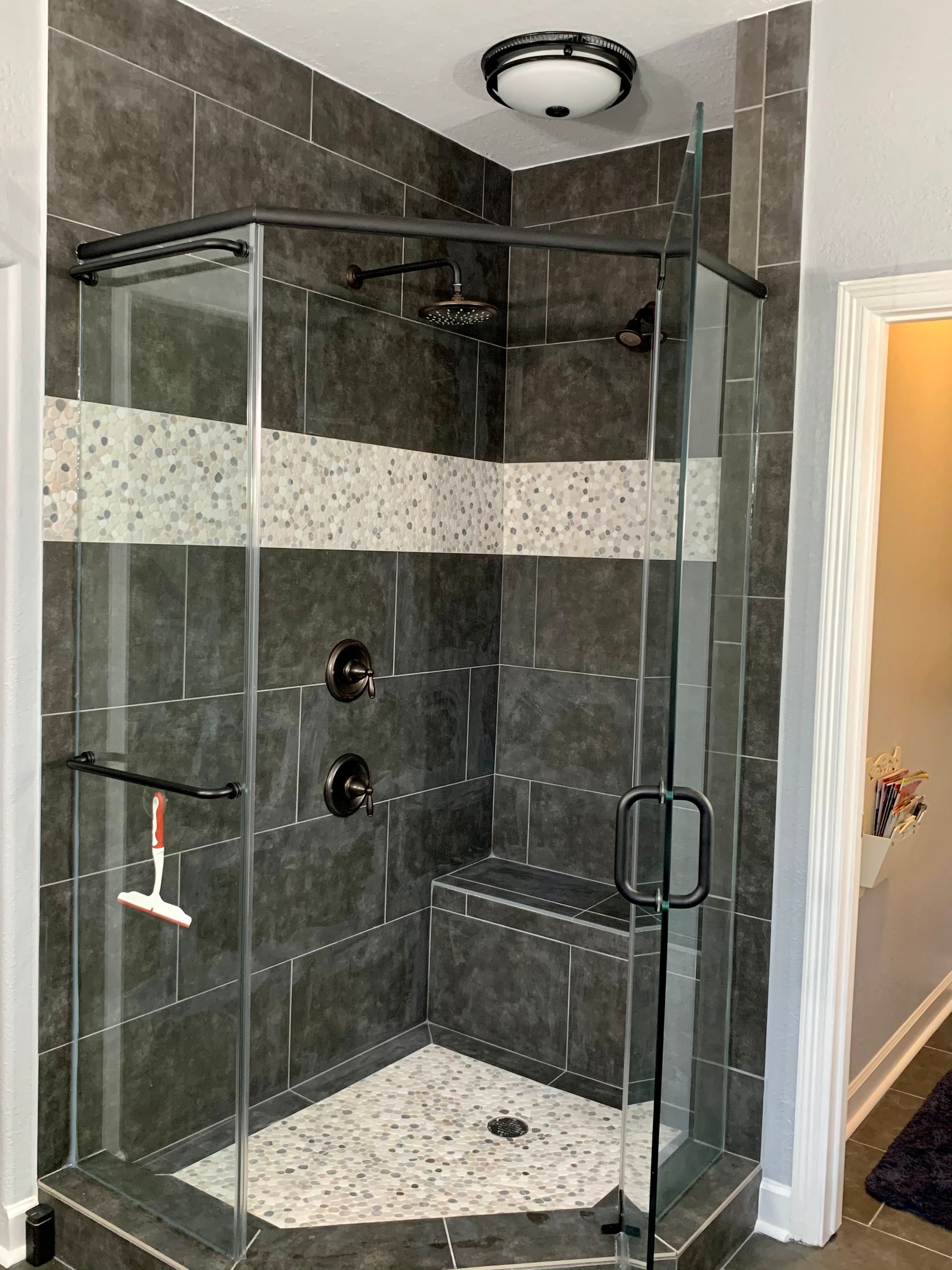 Glass corner shower with gray tile walls and pebble floor in a bathroom