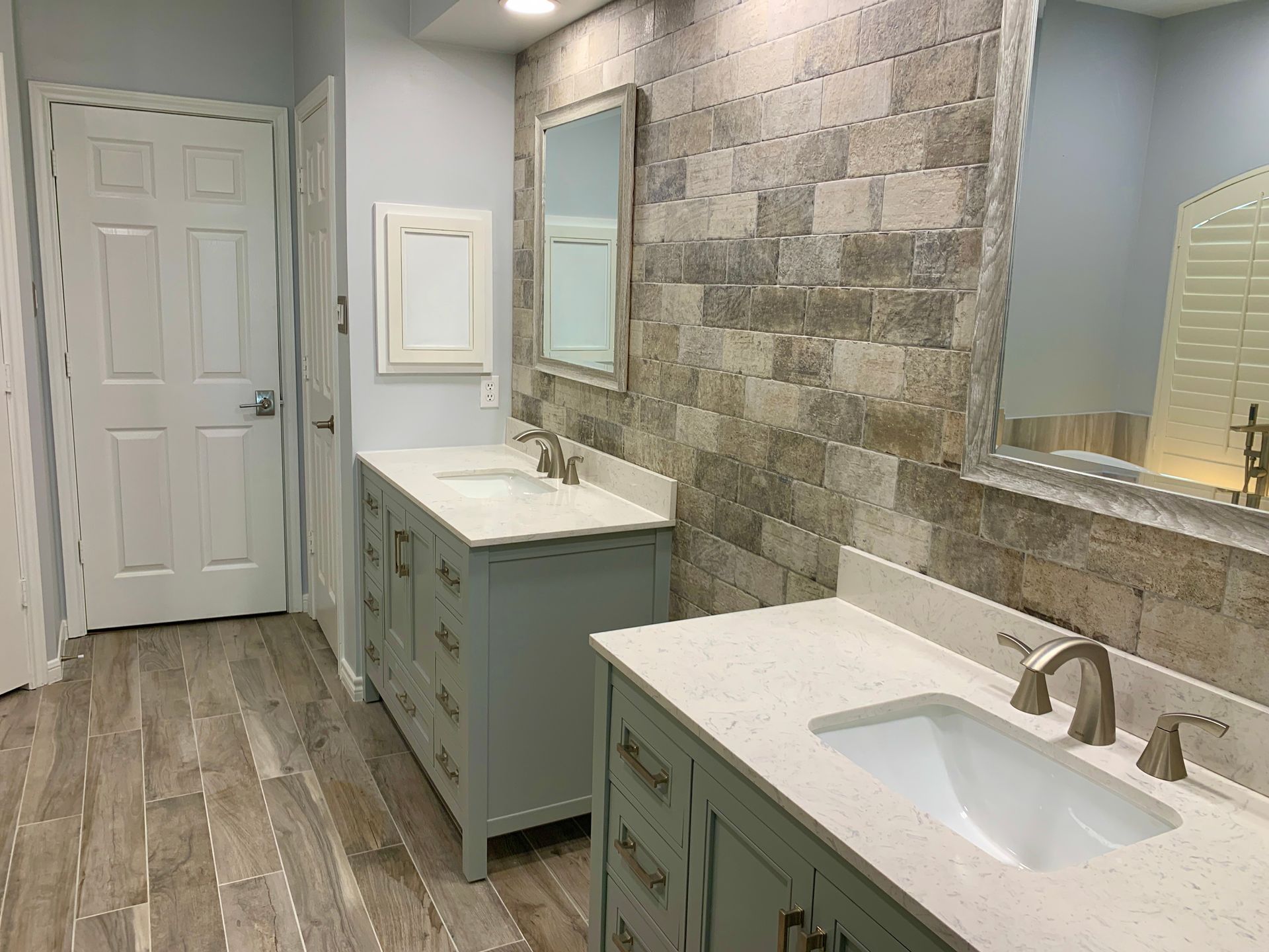 Modern bathroom with double sinks, stone accent wall, and wood-look floor