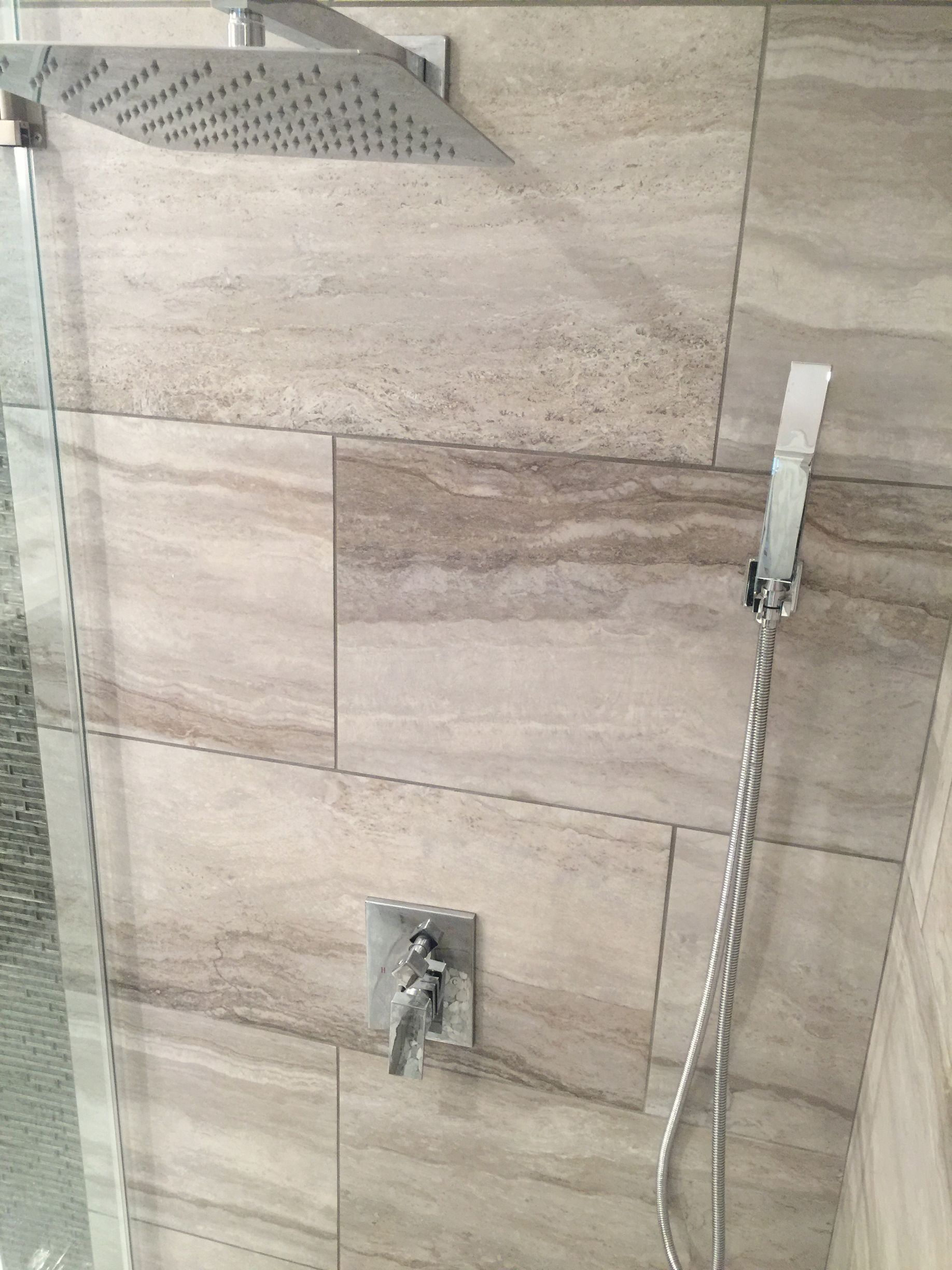 Bathroom shower with beige tile, wall-mounted faucet, and handheld showerhead with hose