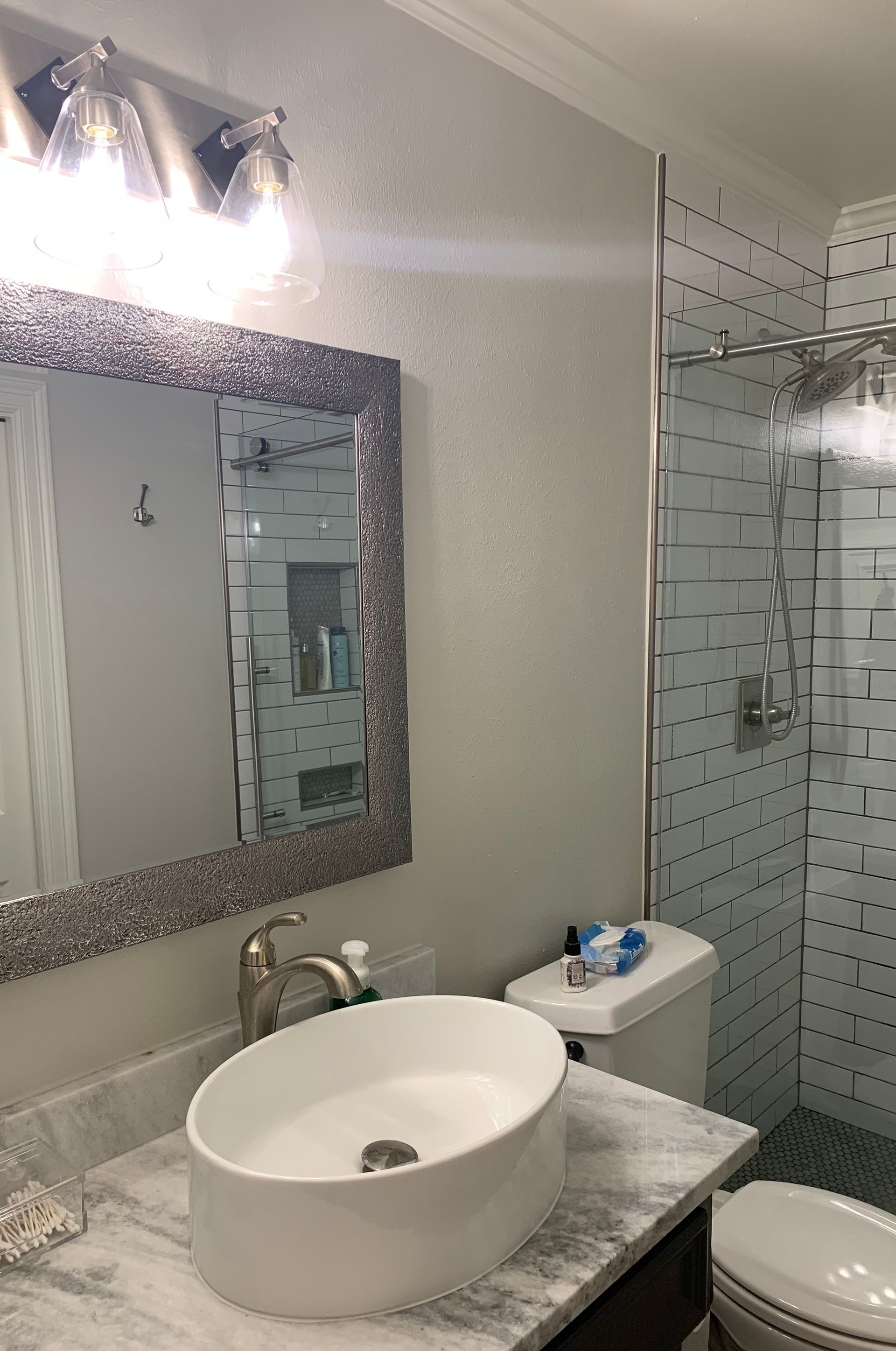 Modern bathroom with marble vanity, round sink, mirror, toilet, and glass shower enclosure.