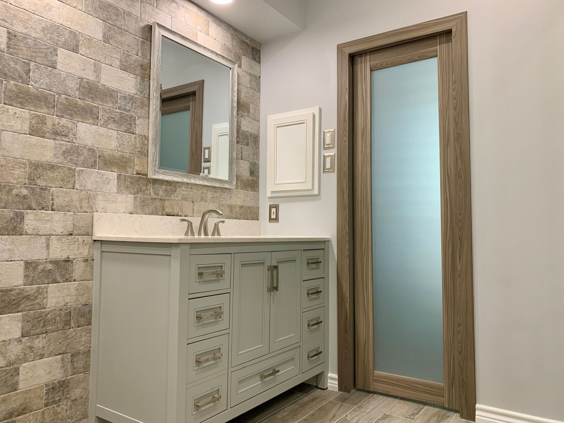 Modern bathroom vanity with a mirrored cabinet, white paneling, and frosted glass door on gray walls