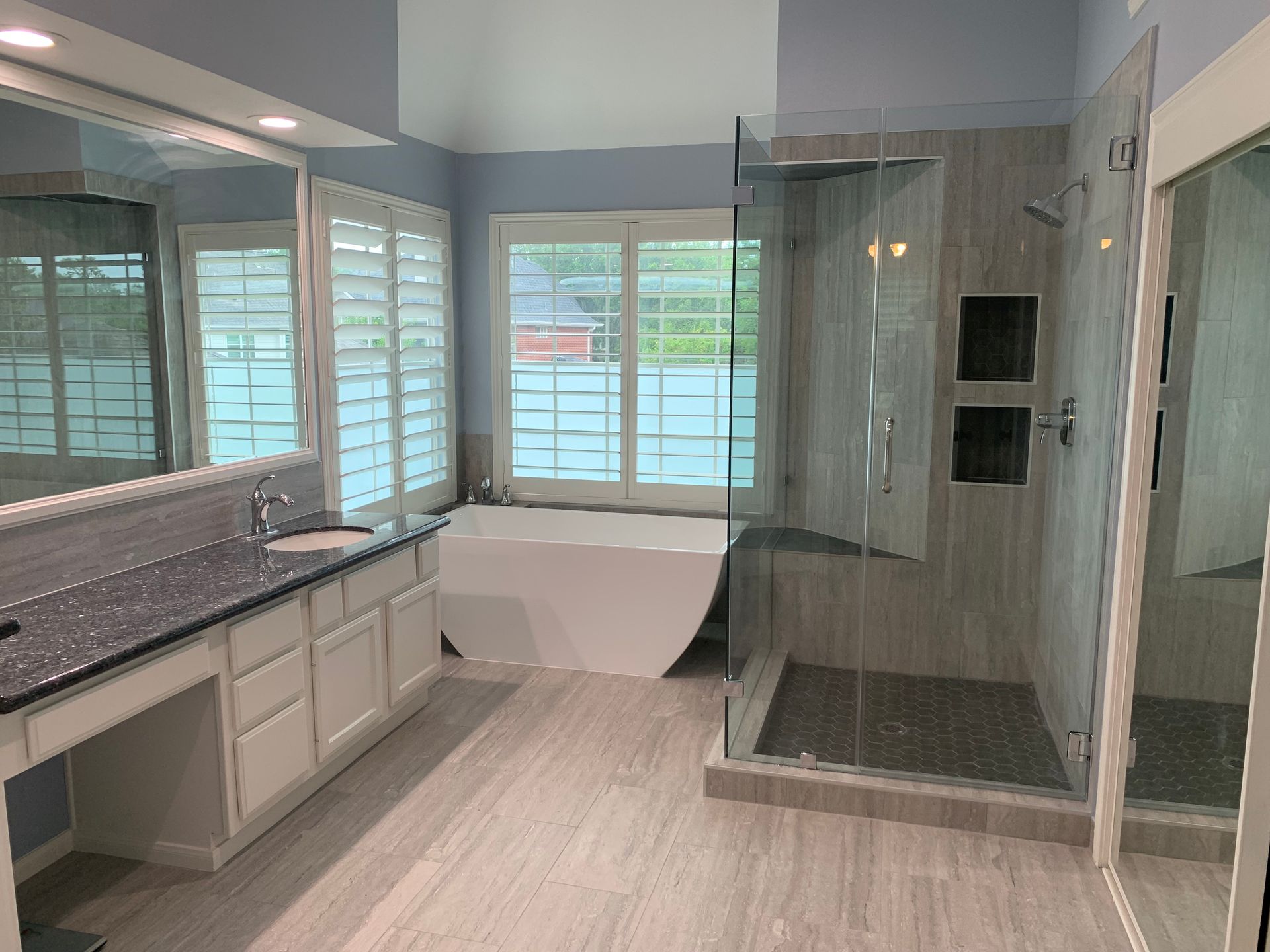 Modern bathroom with double vanity, freestanding tub, glass shower, and light wood floors