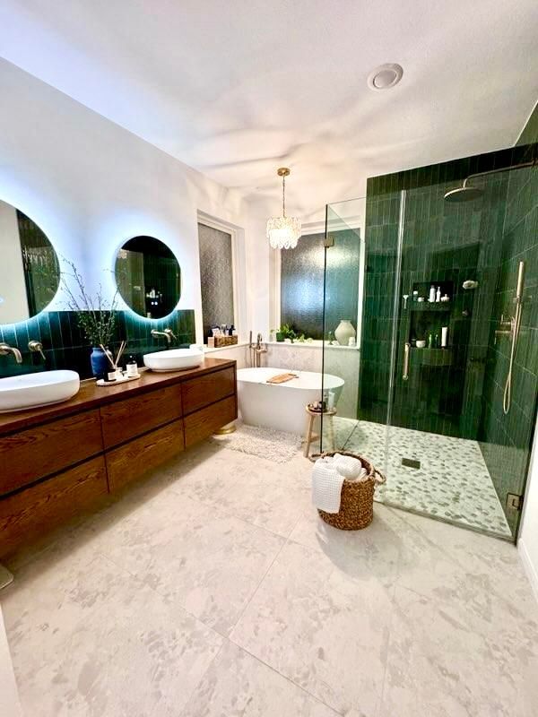 Modern bathroom with green glass shower, floating wood vanity, and round backlit mirrors
