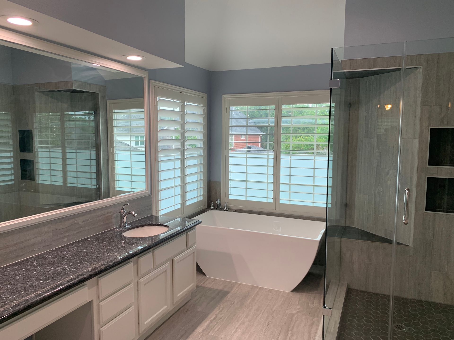 Modern bathroom with double vanity, soaking tub, and glass shower, featuring gray tile and large mirrors.
