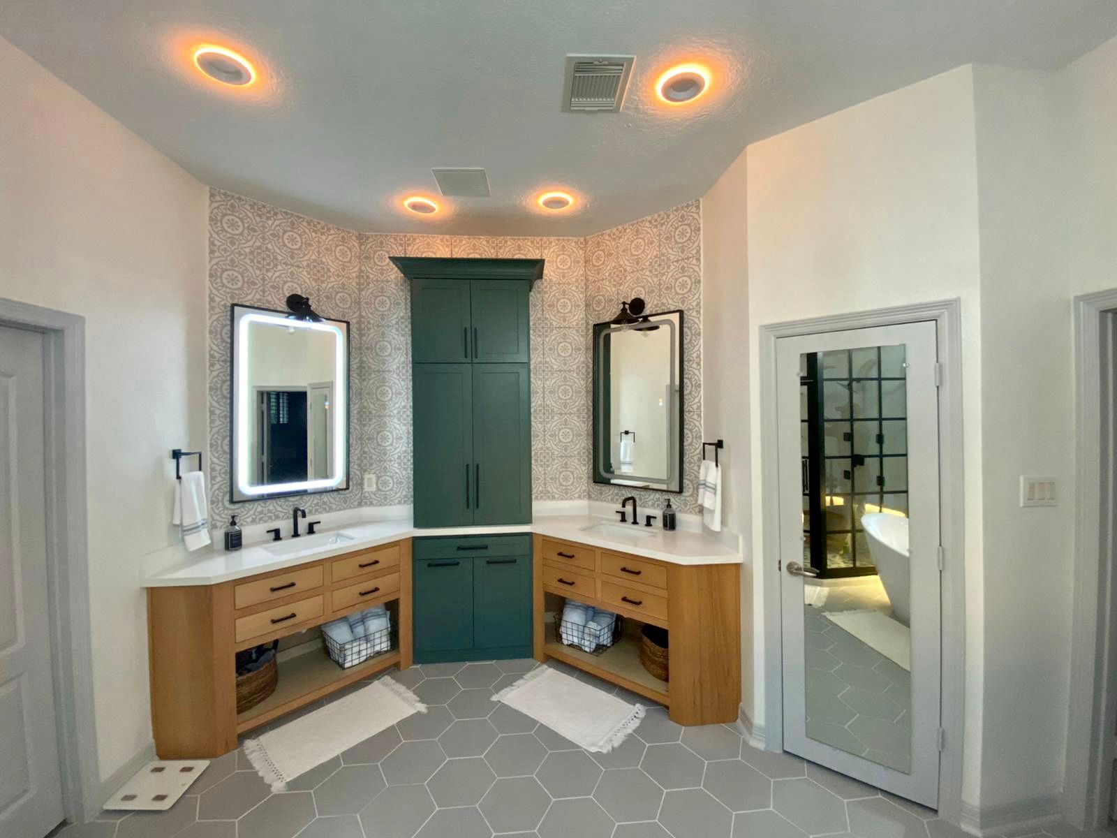 Modern bathroom vanity with two sinks, mirrors, wood cabinets, and teal doors, viewed from the entryway