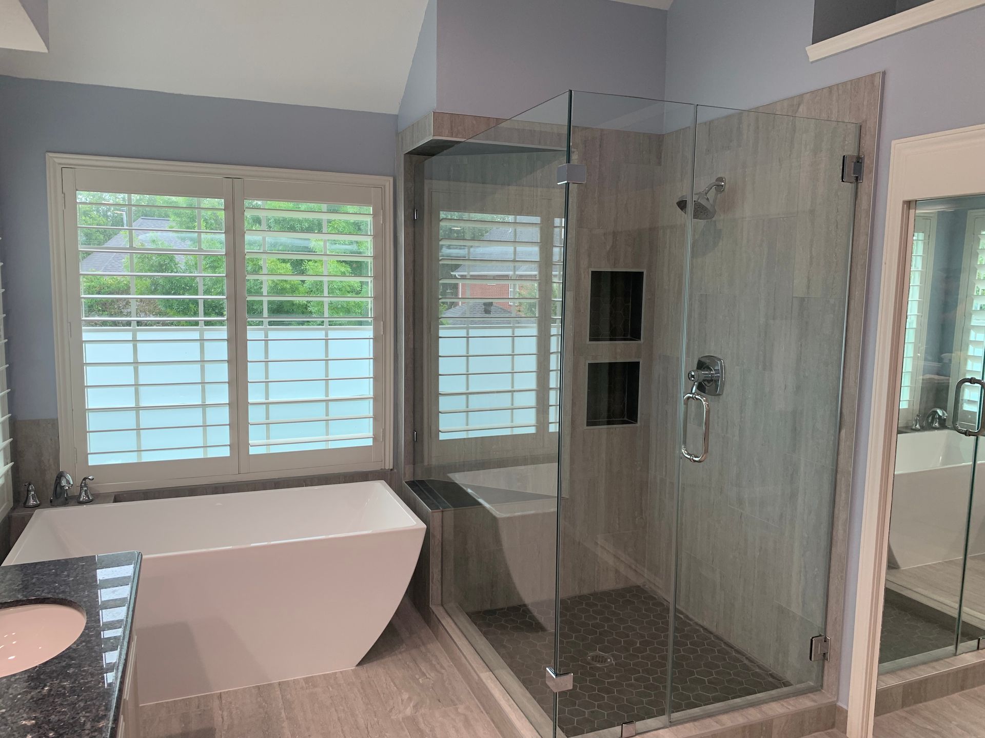 Modern bathroom with a bathtub, glass shower, double windows, and light gray tile walls