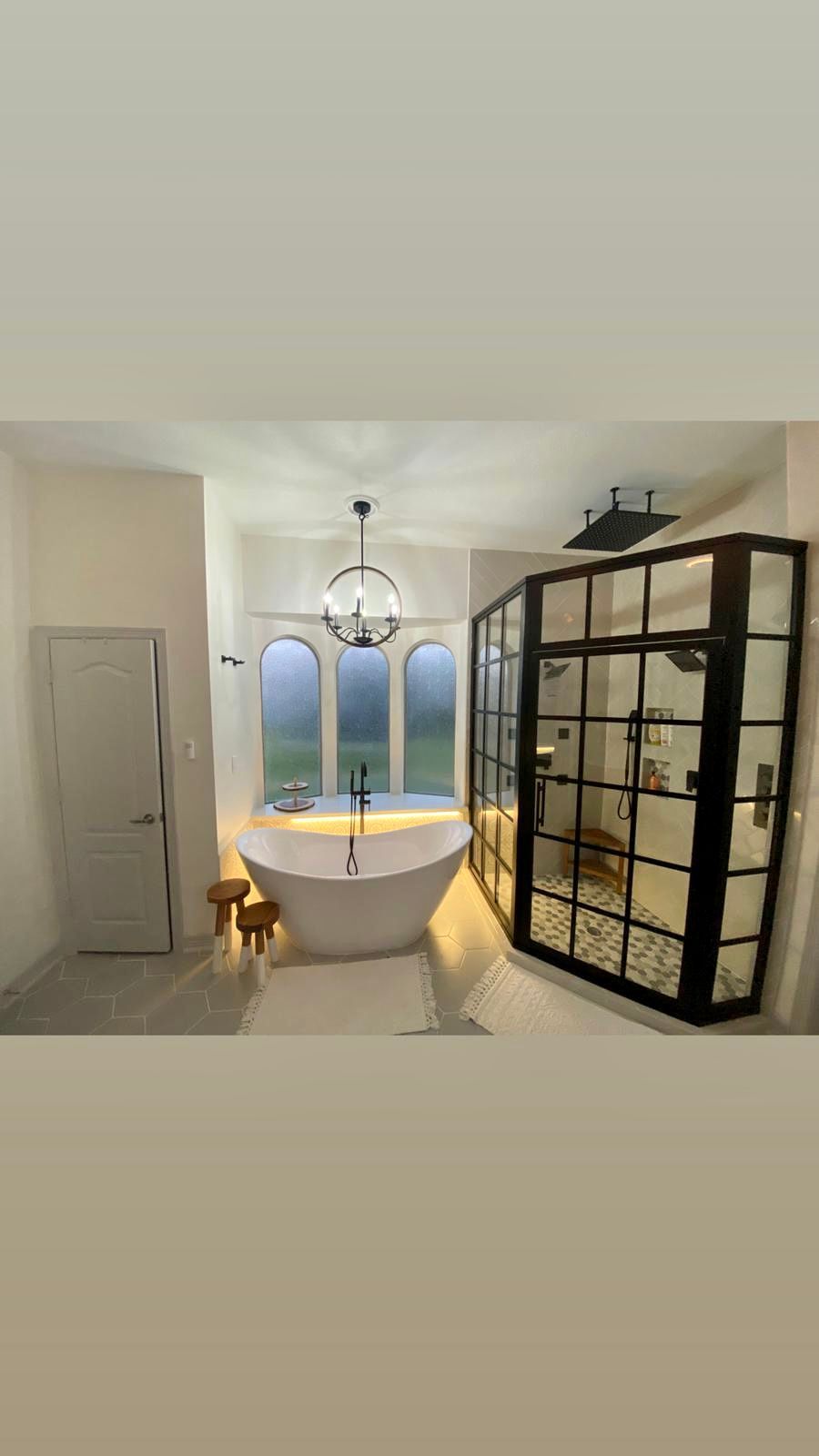 Bright bathroom with freestanding tub, glass shower, chandelier, and a small dog by the door.