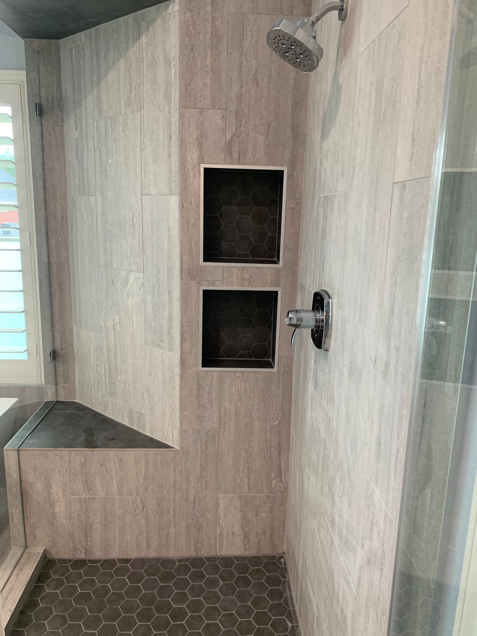Modern bathroom shower with beige tile, glass door, and built-in wall niches