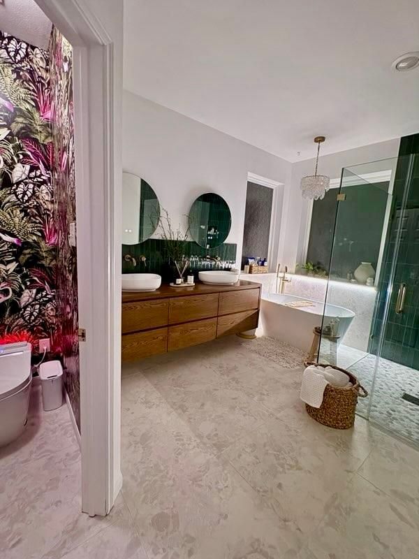 Bright bathroom with white walls, wooden vanity, arched mirrors, glass shower, and floral decor nearby