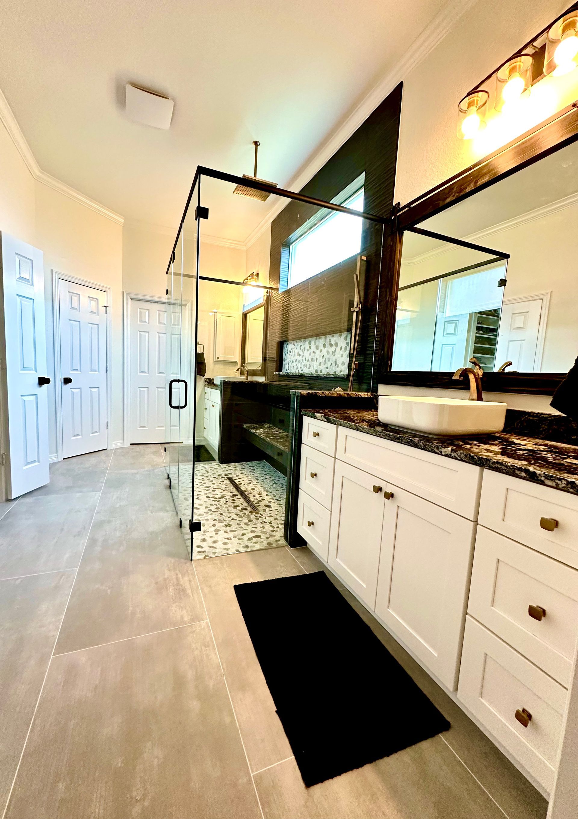 Modern bathroom with black-framed glass shower, white vanity, and large mirror with warm lighting