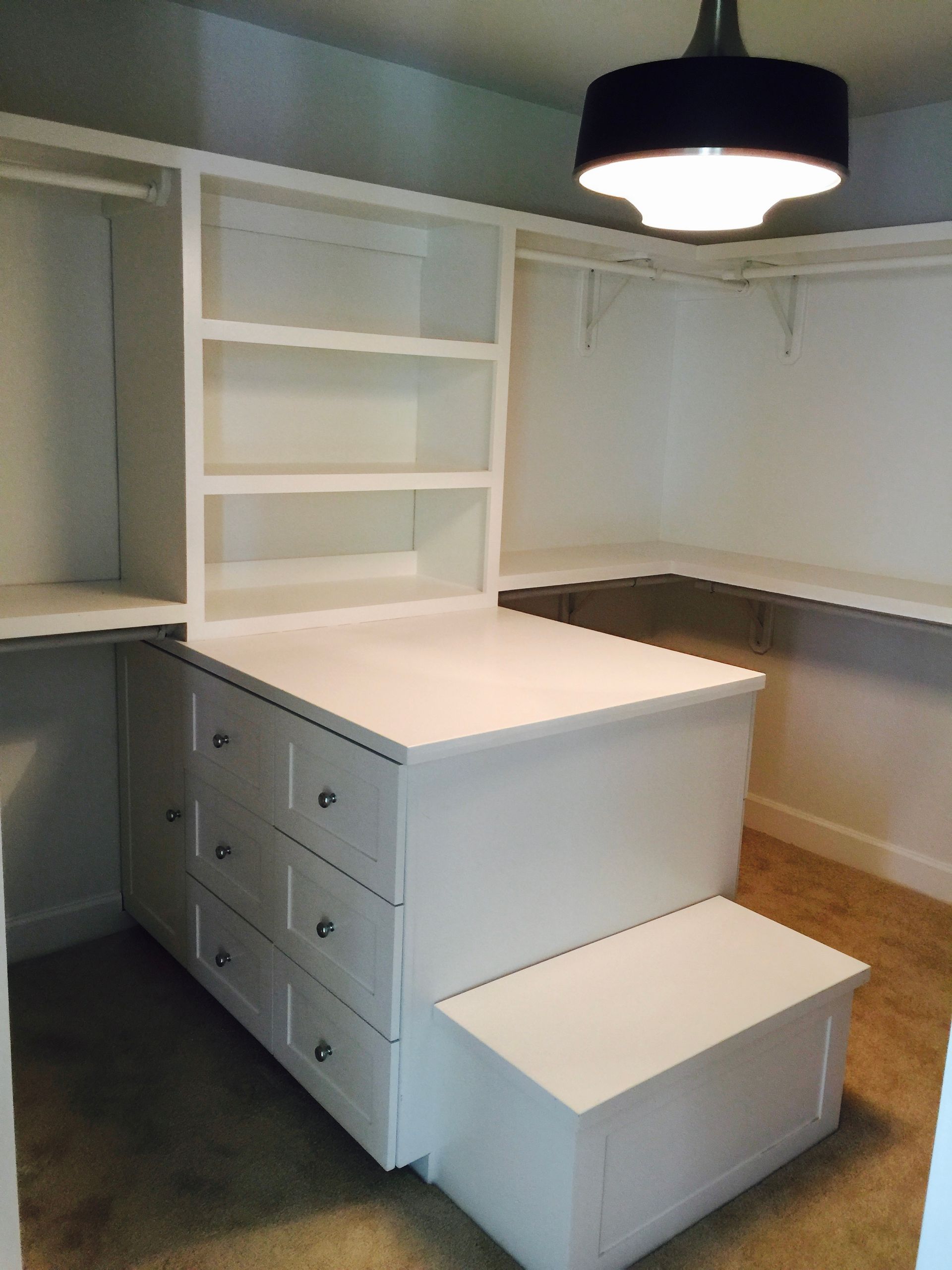 White built-in desk with drawers, shelves, and bench in a small room with a hanging light fixture