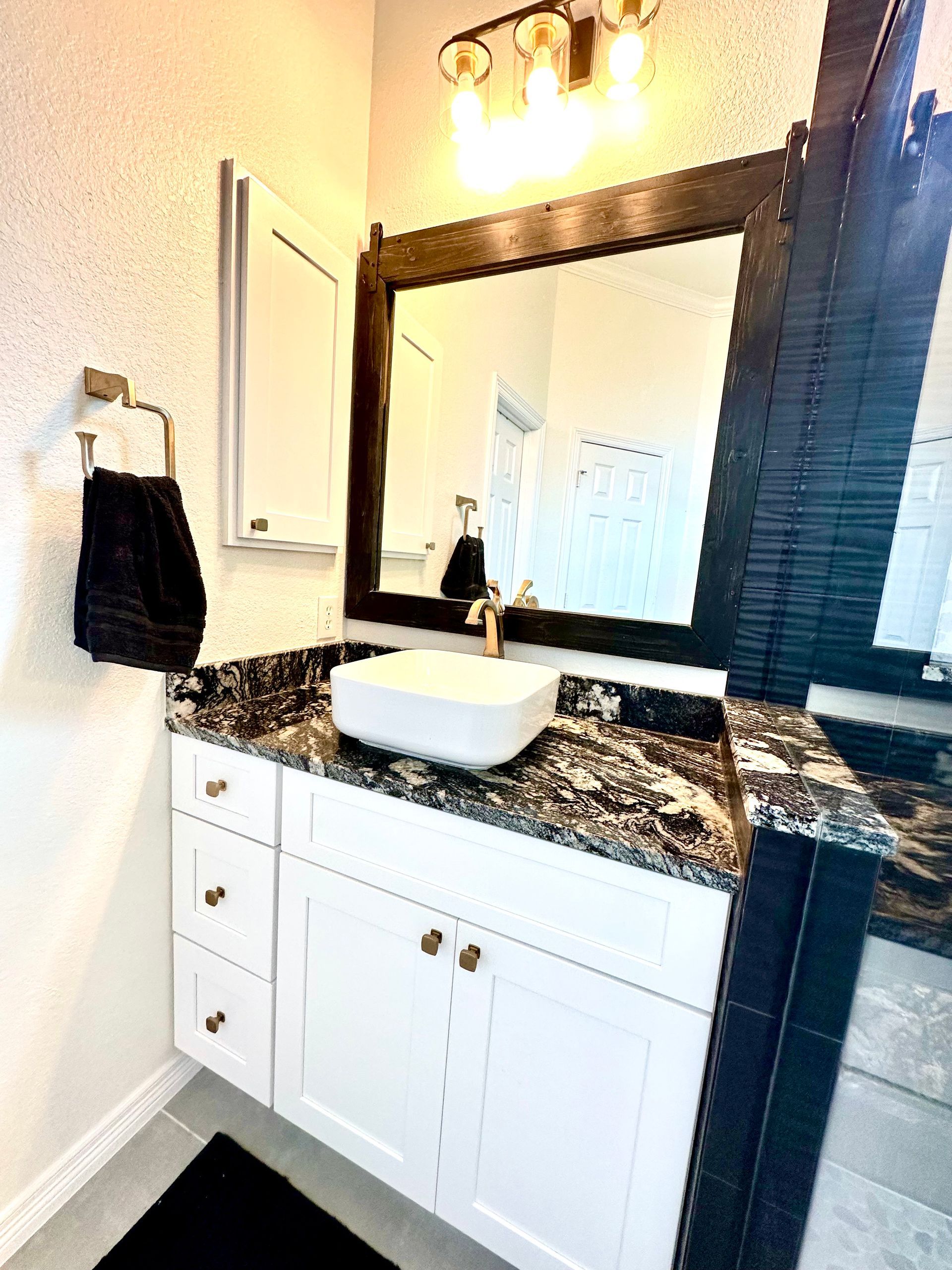 Bathroom vanity with white cabinet, black granite countertop, square vessel sink, and wall mirror beneath lights