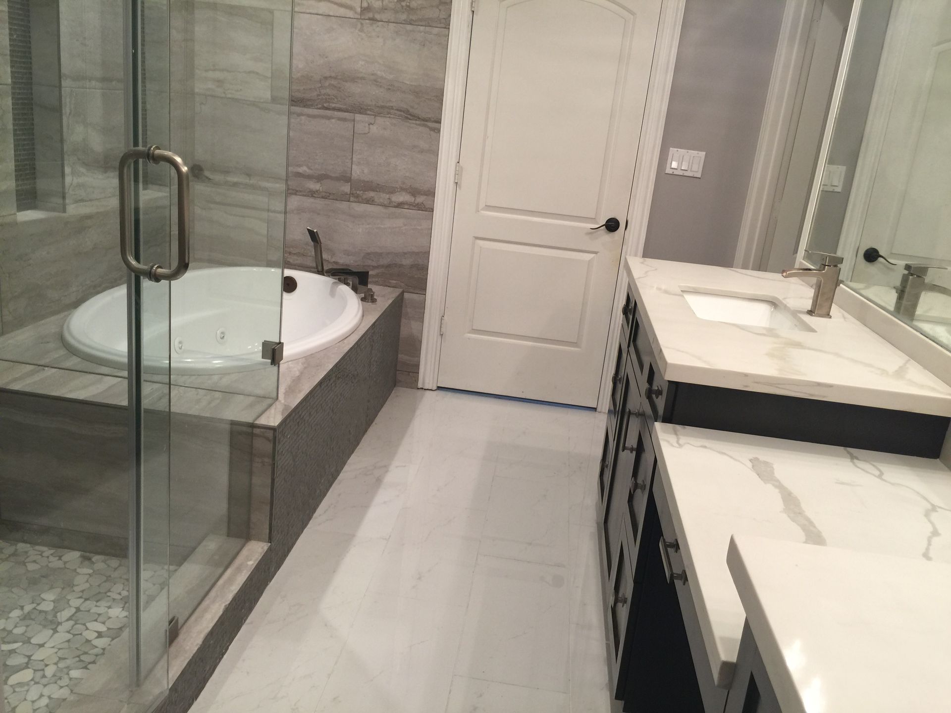 Modern bathroom with glass shower, soaking tub, double vanity, and gray tile walls