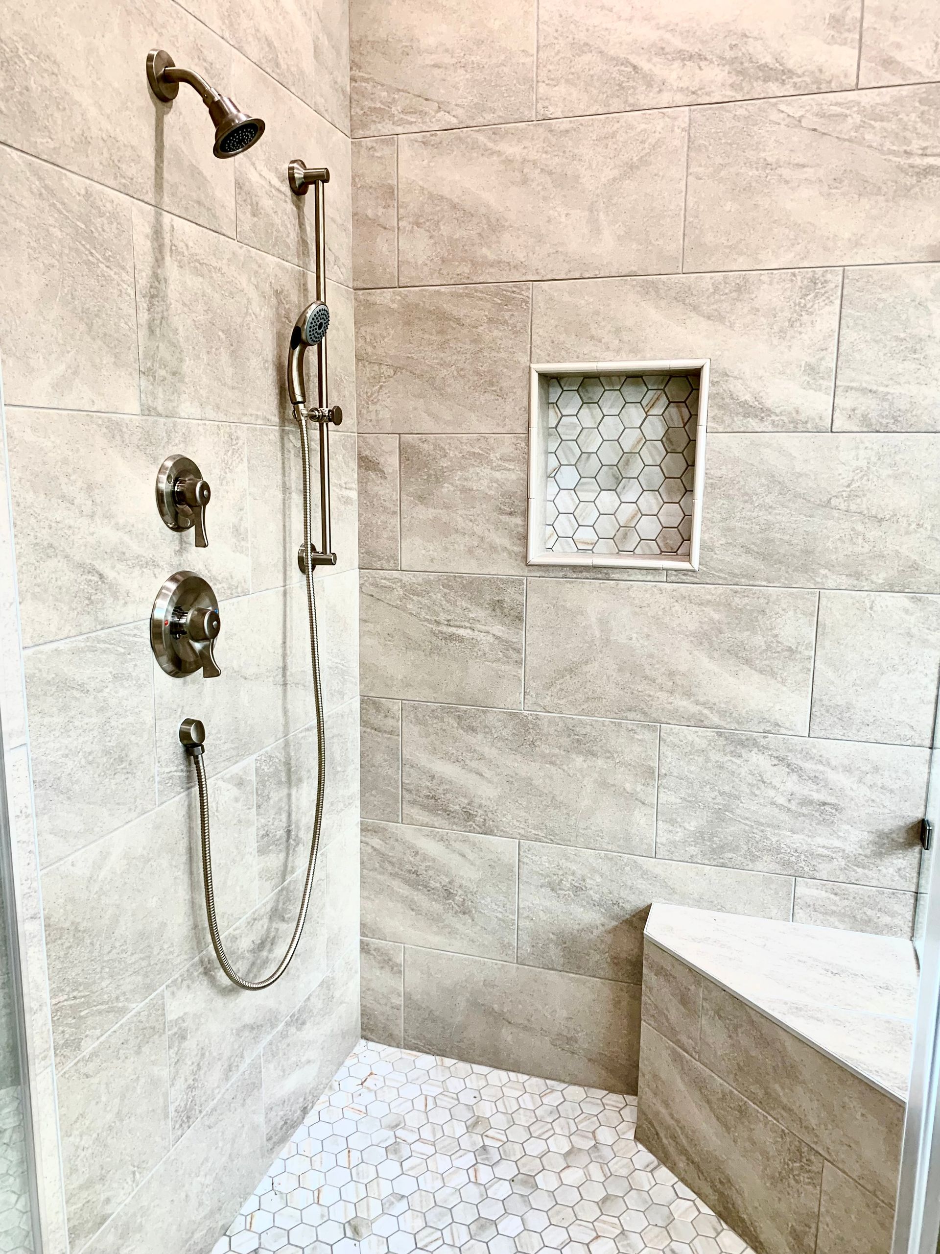 Stone-tiled shower with dual showerheads, built-in niche, and white pebble floor.