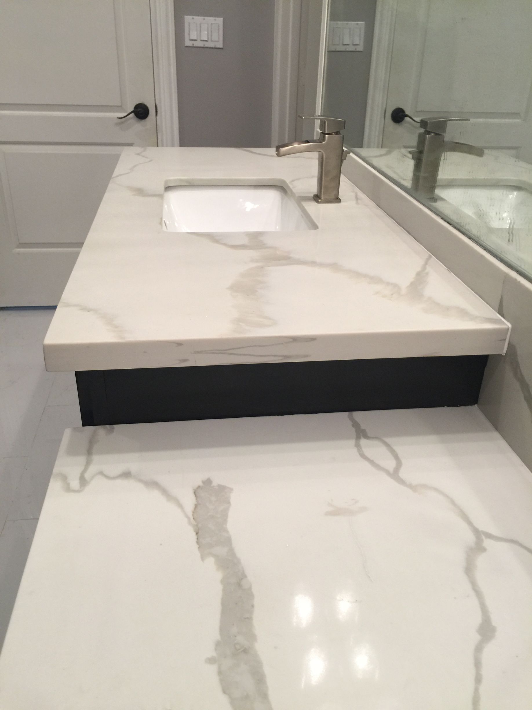 Modern bathroom vanity with white marble countertop, rectangular sink, and chrome faucet, with mirror and shower wall nearby
