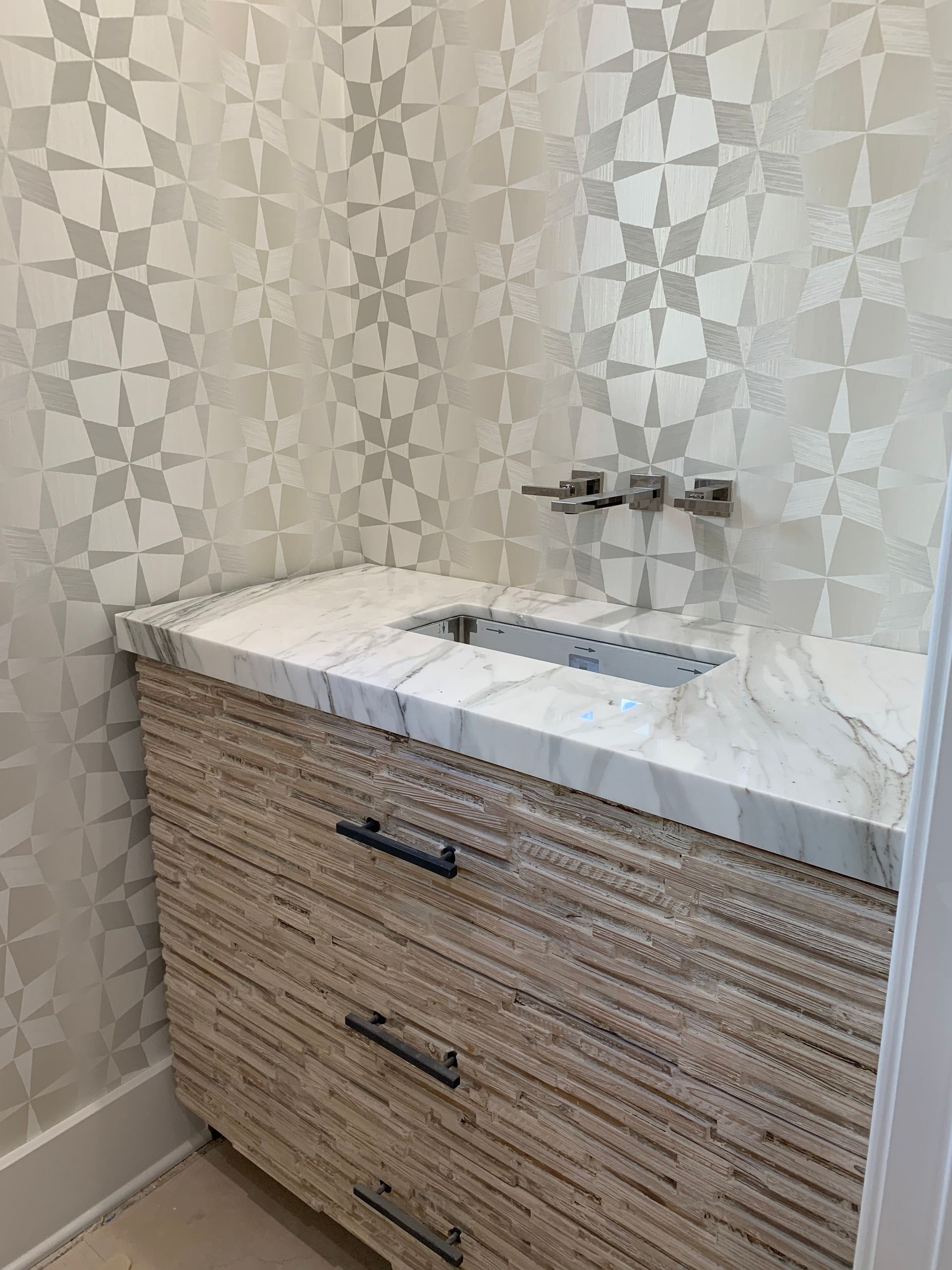 Bathroom vanity with marble sink, wall-mounted faucets, and light patterned wallpaper
