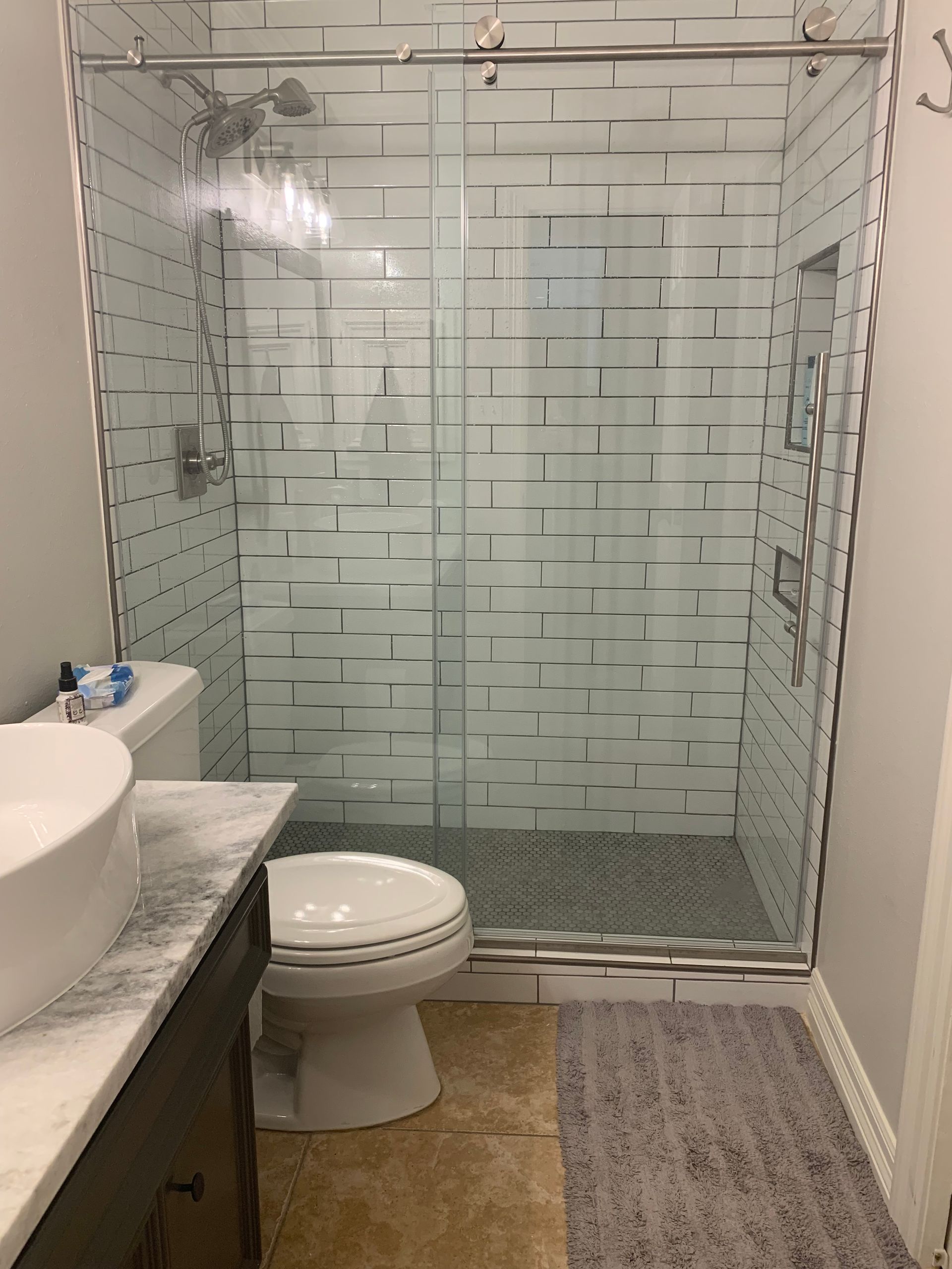 Bathroom with glass walk-in shower, toilet, sink, and gray striped rug.