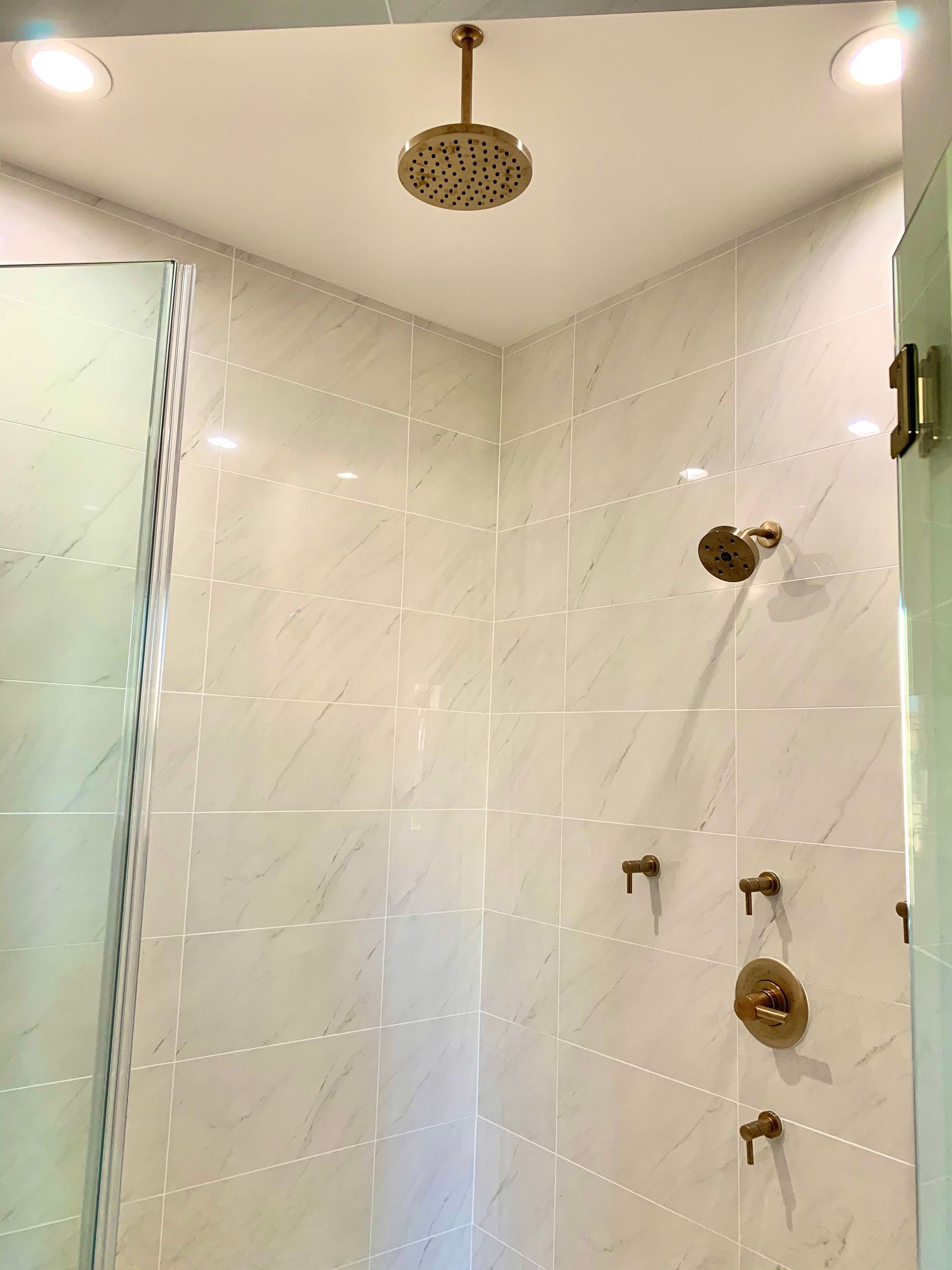 Modern white tiled shower with brass fixtures and overhead rainfall showerhead