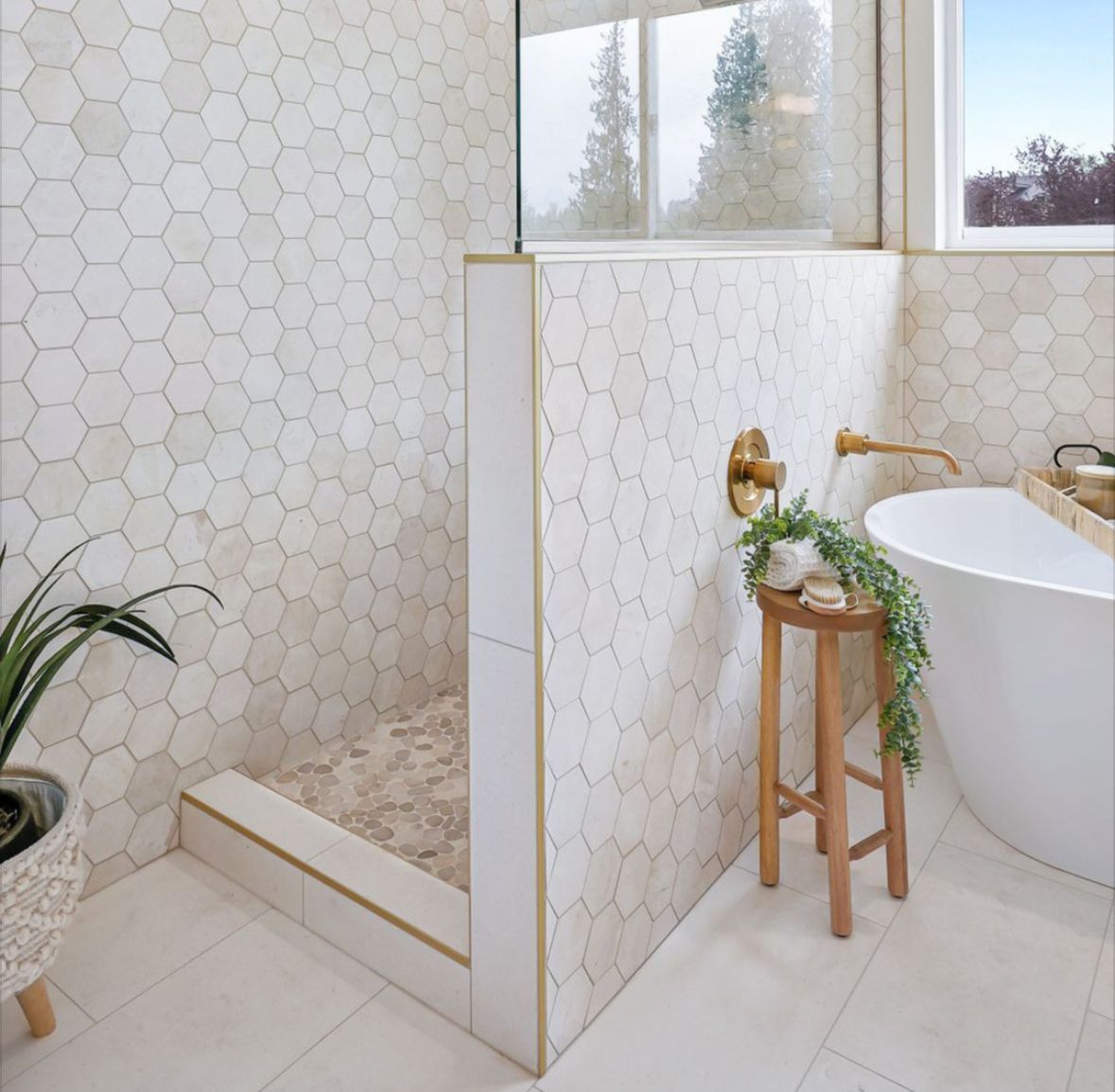 Bright modern bathroom with freestanding tub, walk-in shower, gold fixtures, and potted plant.