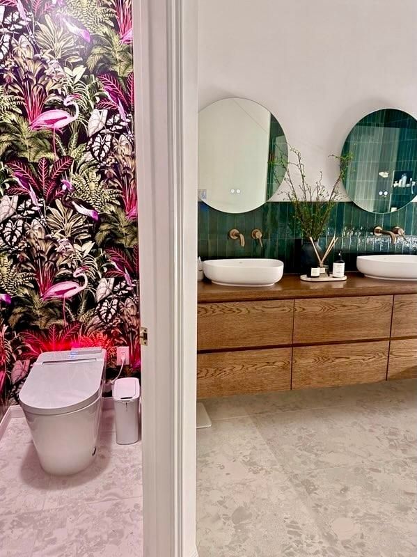 Modern bathroom with floral wall, white toilet, and wooden vanity with round mirrors