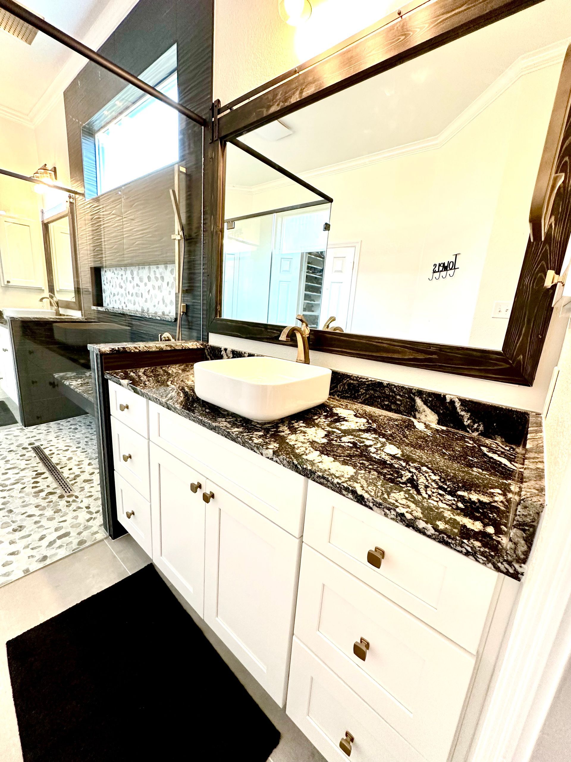 Modern bathroom vanity with granite countertop, white cabinets, sink, and large mirror in a bright interior