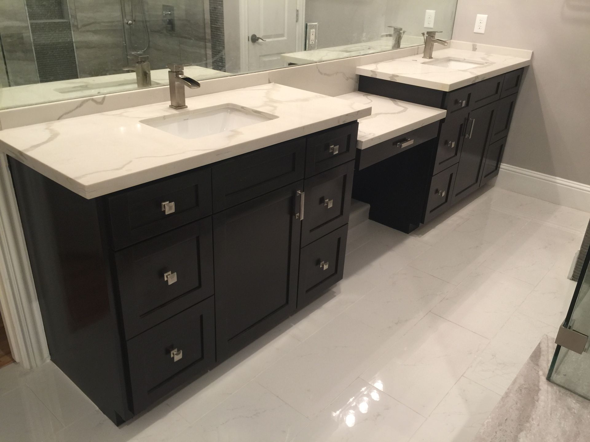 Bathroom with two dark vanity cabinets, white countertops, and large mirrors along a light tiled wall