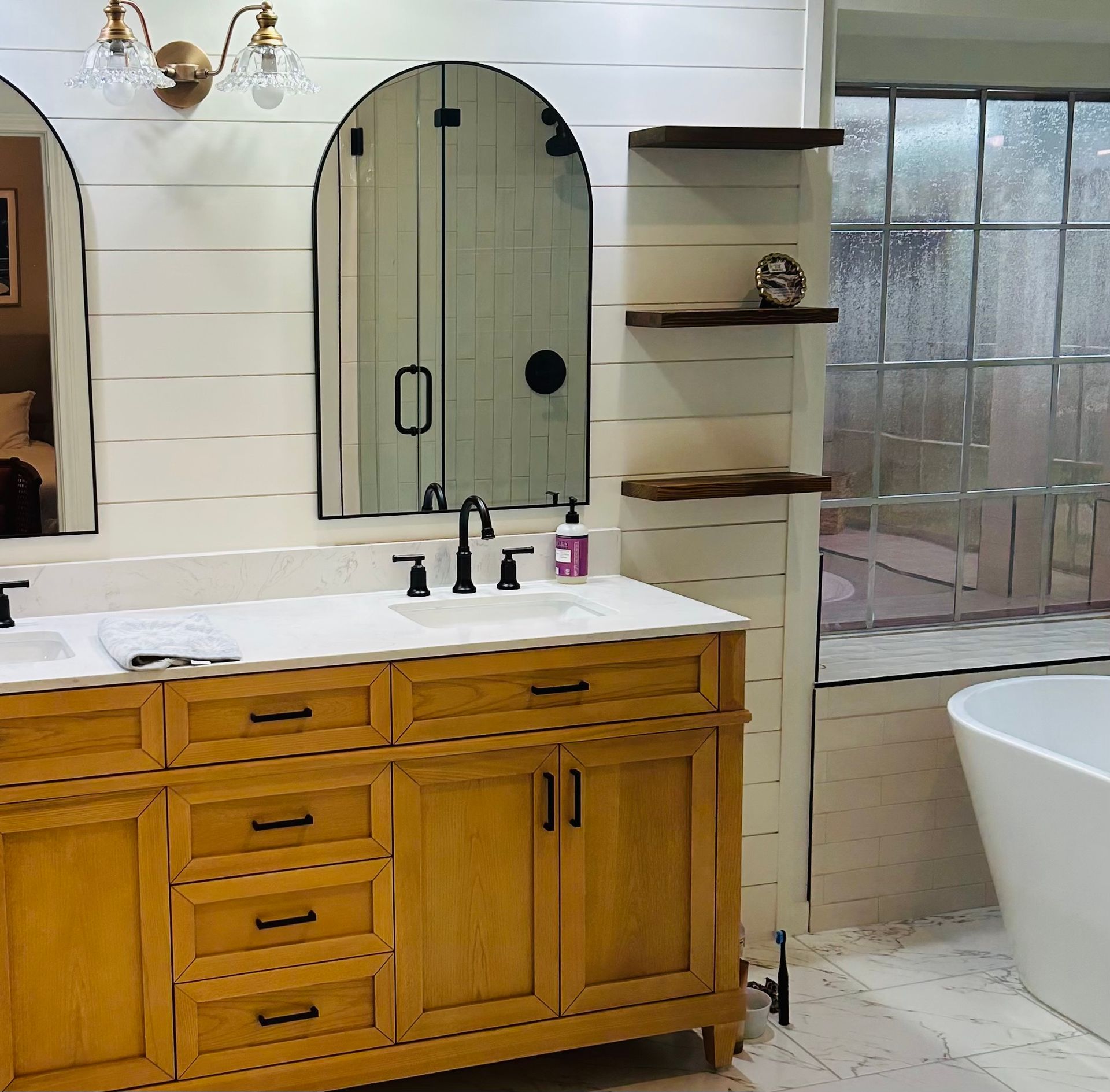Rustic bathroom with wood vanity, arched mirror, shower shelf, and frosted glass window