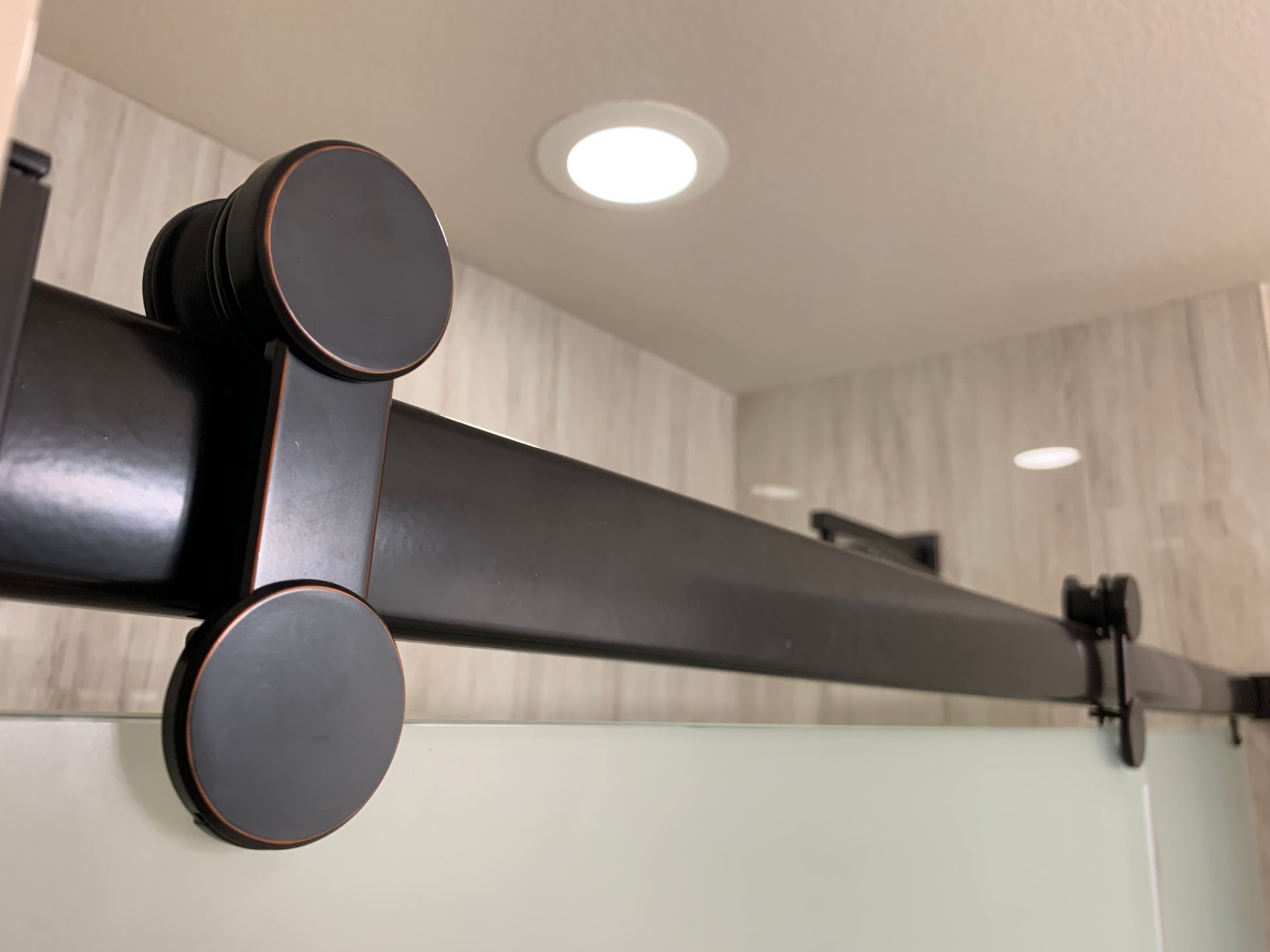 Black sliding shower door track with round rollers mounted under a ceiling light