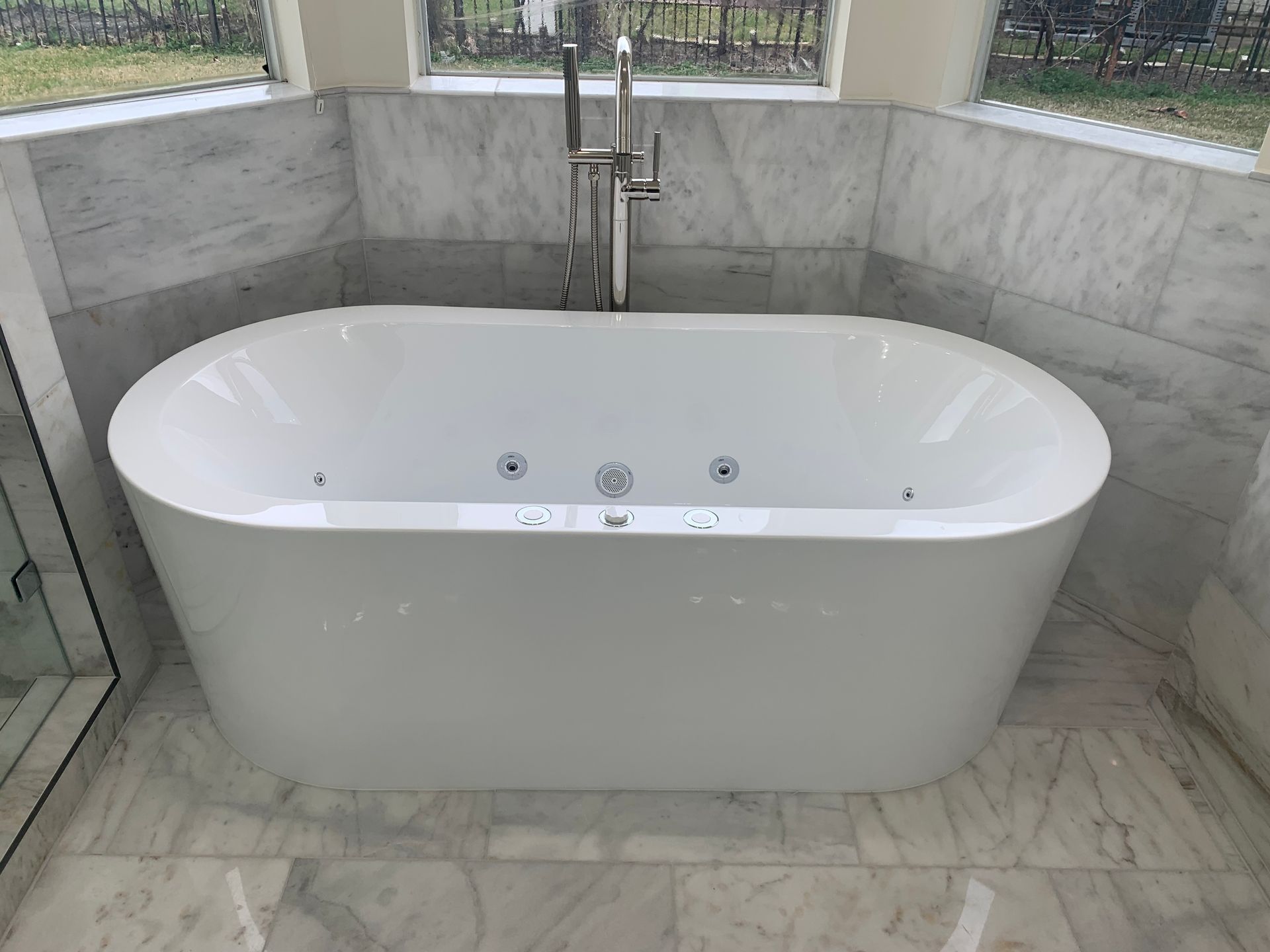 Freestanding white bathtub in a tiled bathroom with a wall-mounted faucet and shower