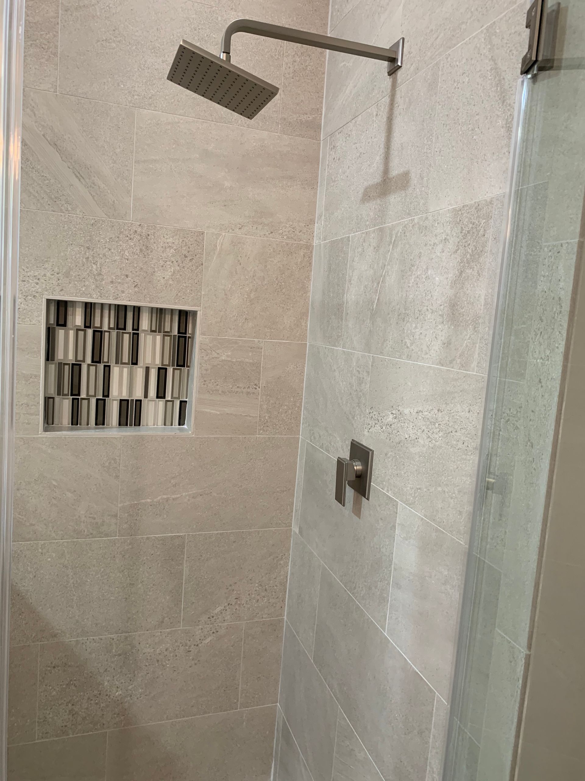 Modern shower with beige tile walls, square rain showerhead, and built-in accent tile niche.