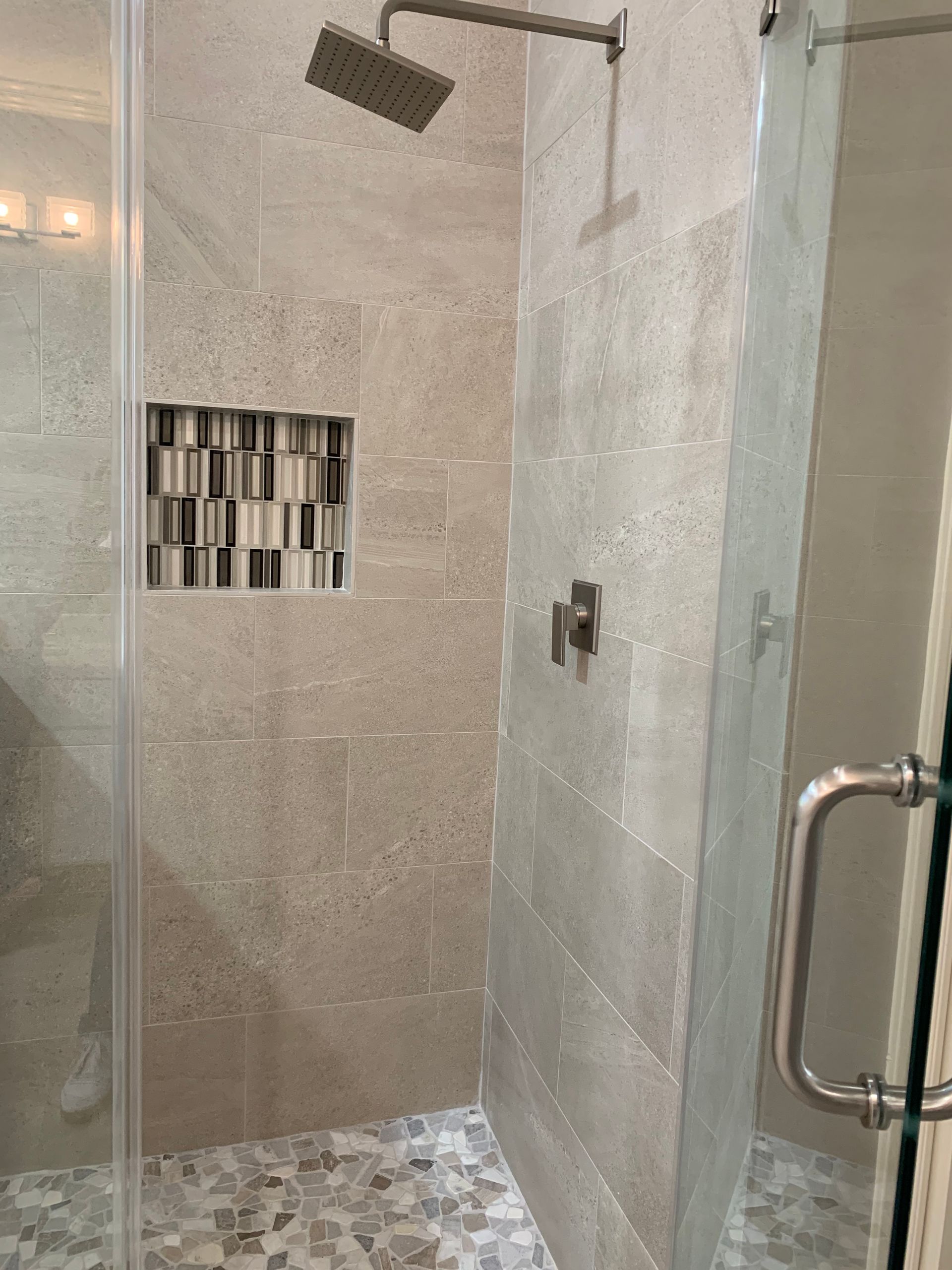 Modern tiled shower with glass door, chrome handle, rainfall showerhead, and mosaic accent tile.