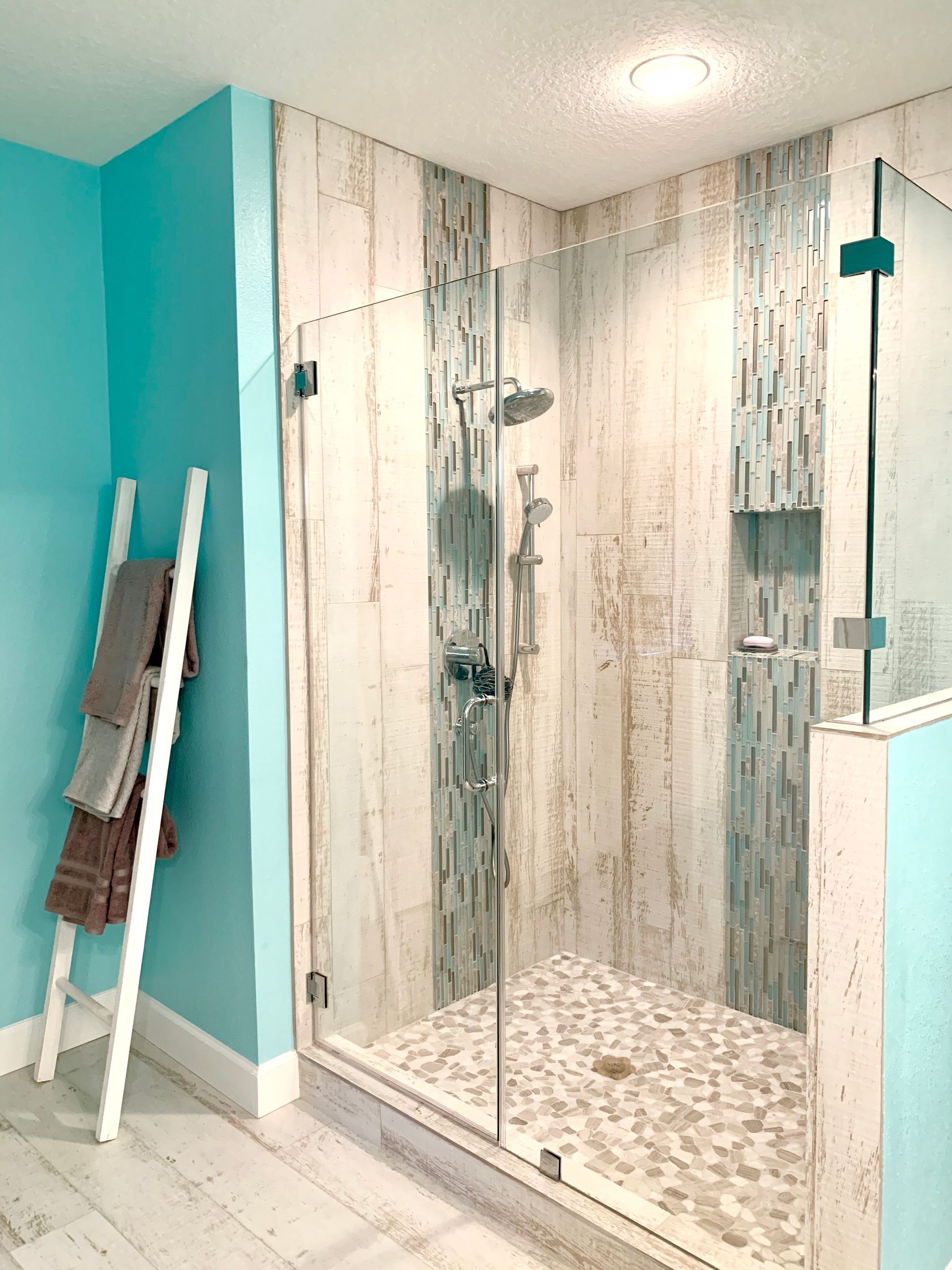 Modern bathroom shower with glass doors, white wood-look tiles, turquoise walls, and a hanging towel ladder
