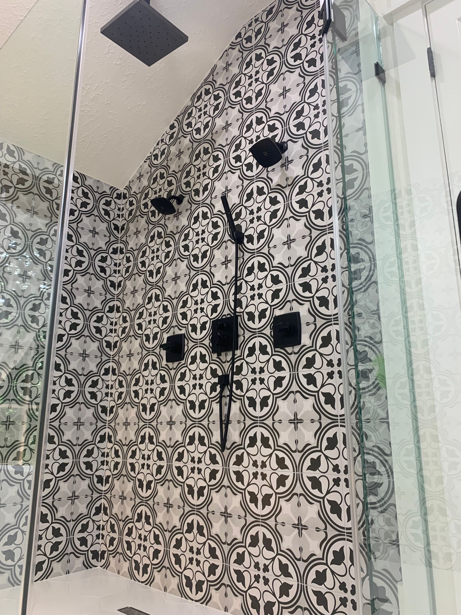 Patterned bathroom shower with black-and-white tile, glass partition, and overhead showerhead