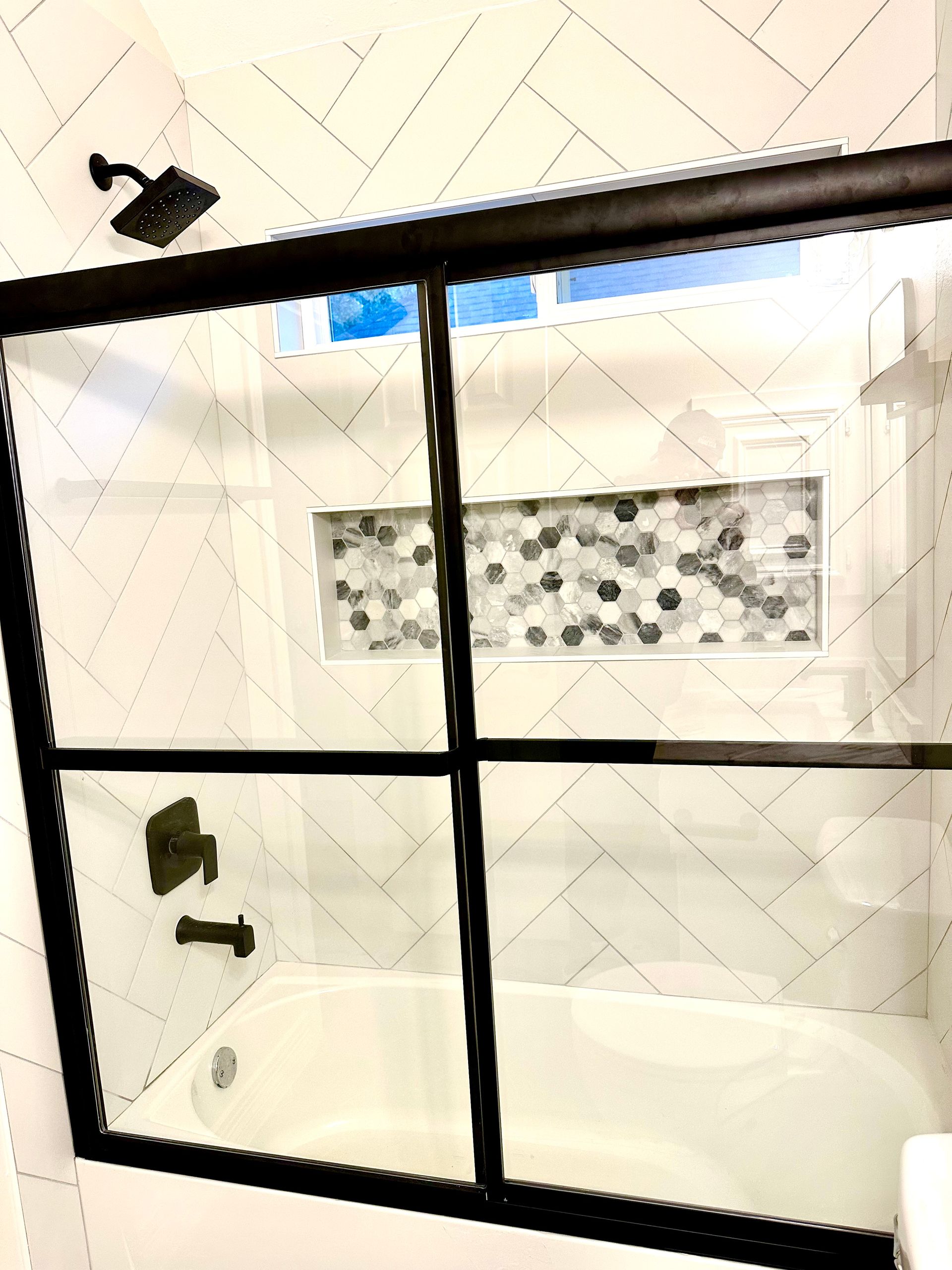 Black-framed glass shower enclosure in a bright bathroom with white tiled walls.