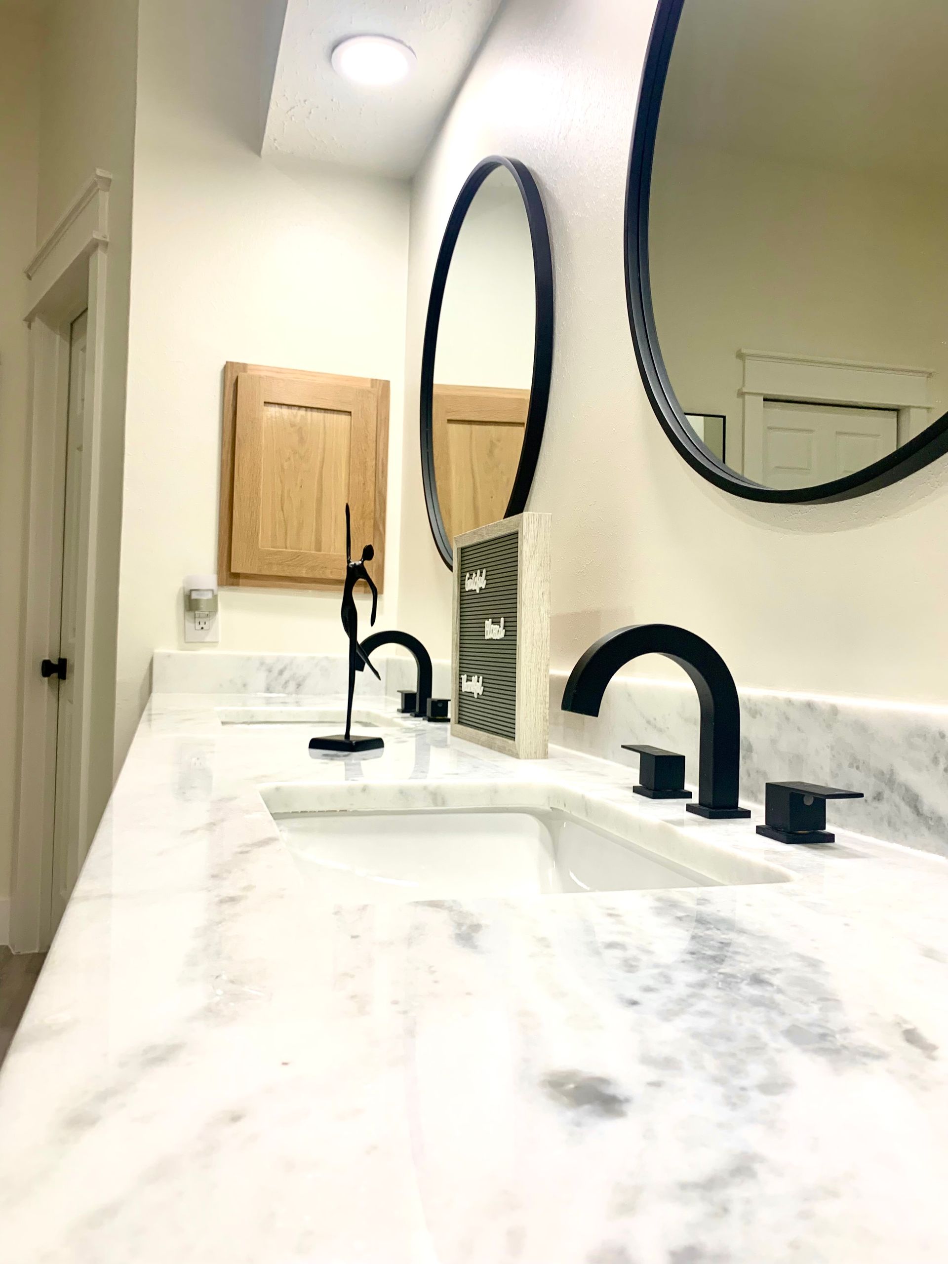 Bright bathroom vanity with white marble countertop, two sinks, black faucets, and oval mirrors