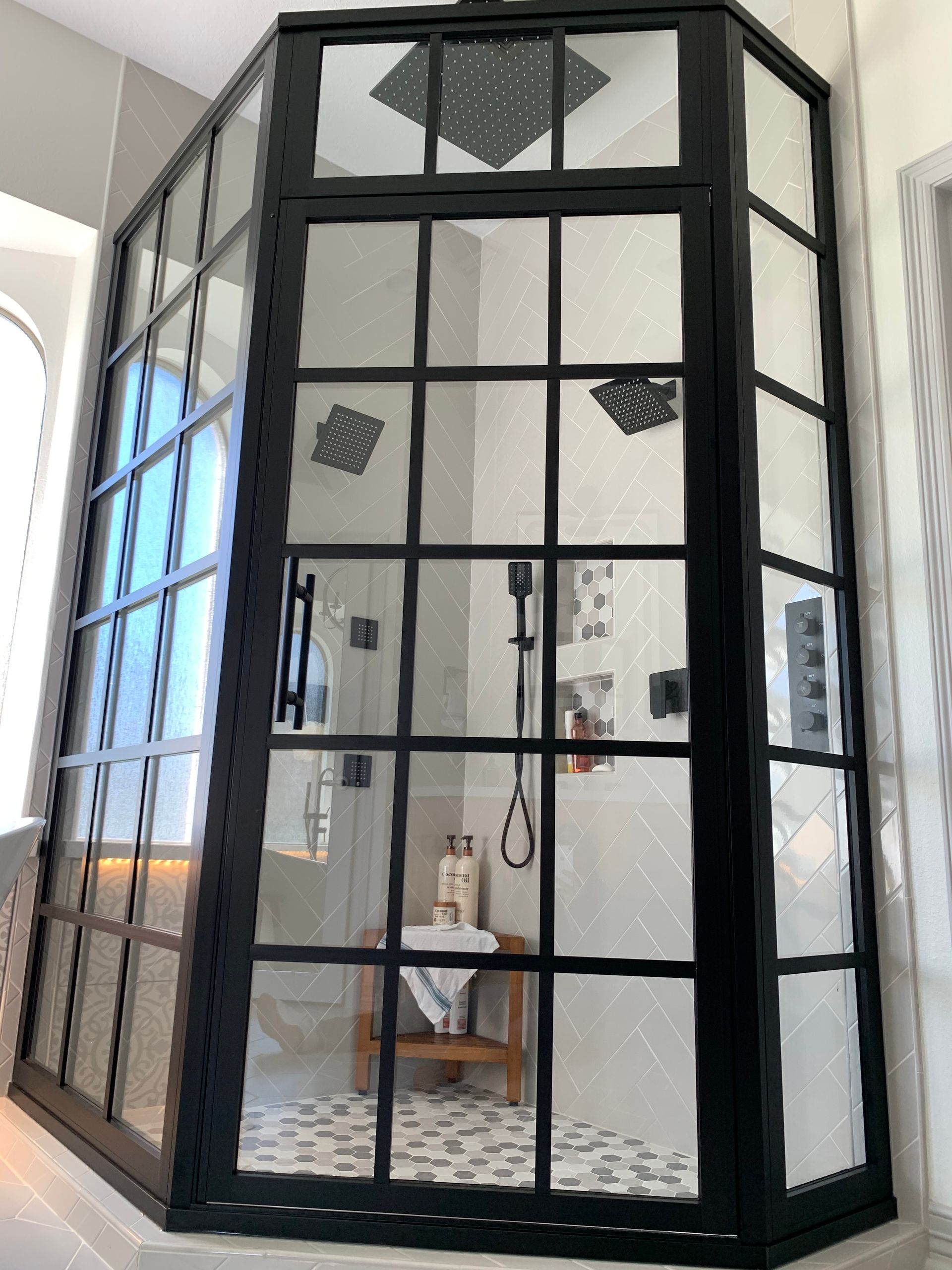 Black-framed glass shower enclosure with patterned tile floor in a bright bathroom