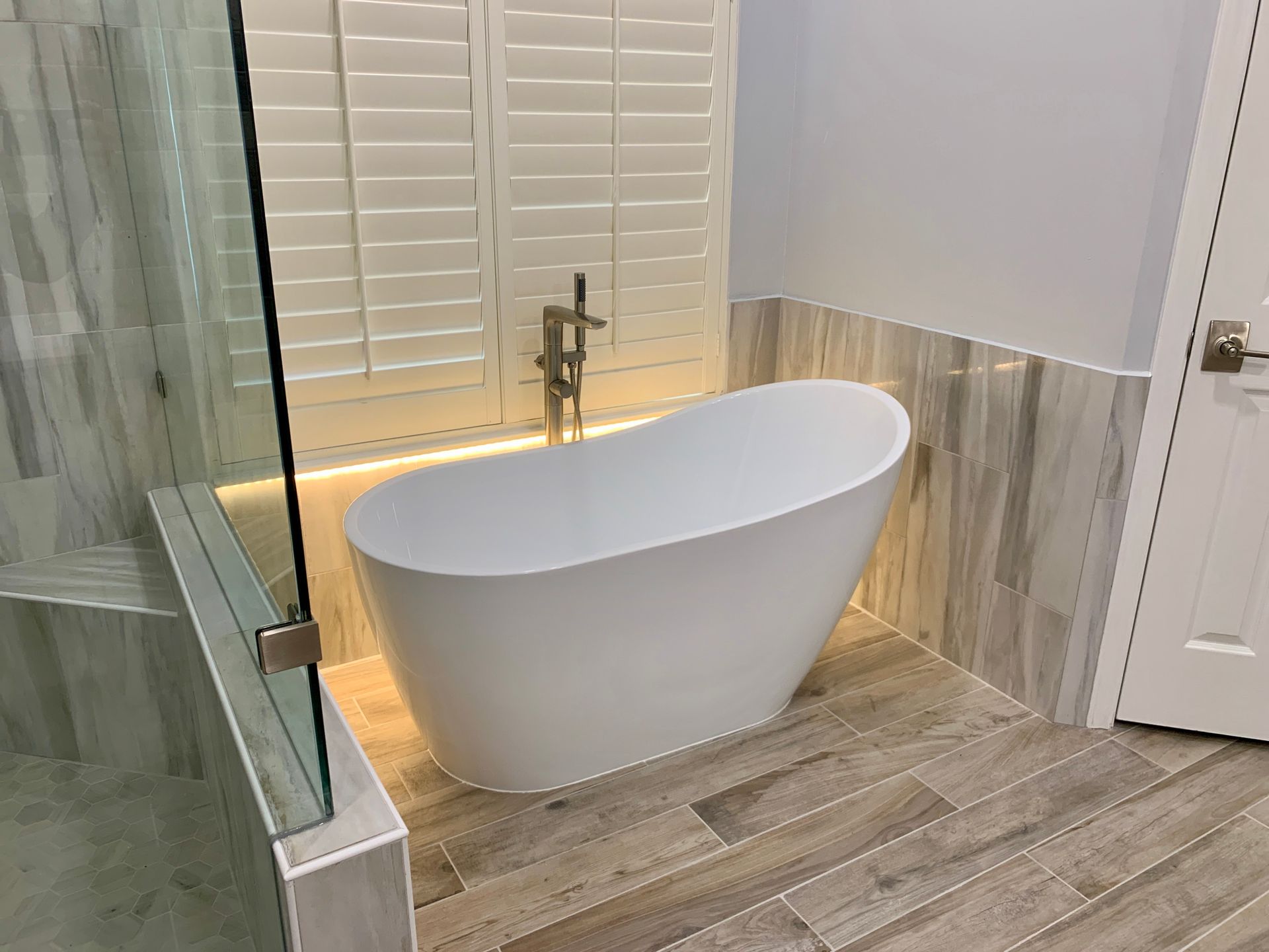 Modern bathroom with a freestanding white tub, glass shower, and wood-look tile floor