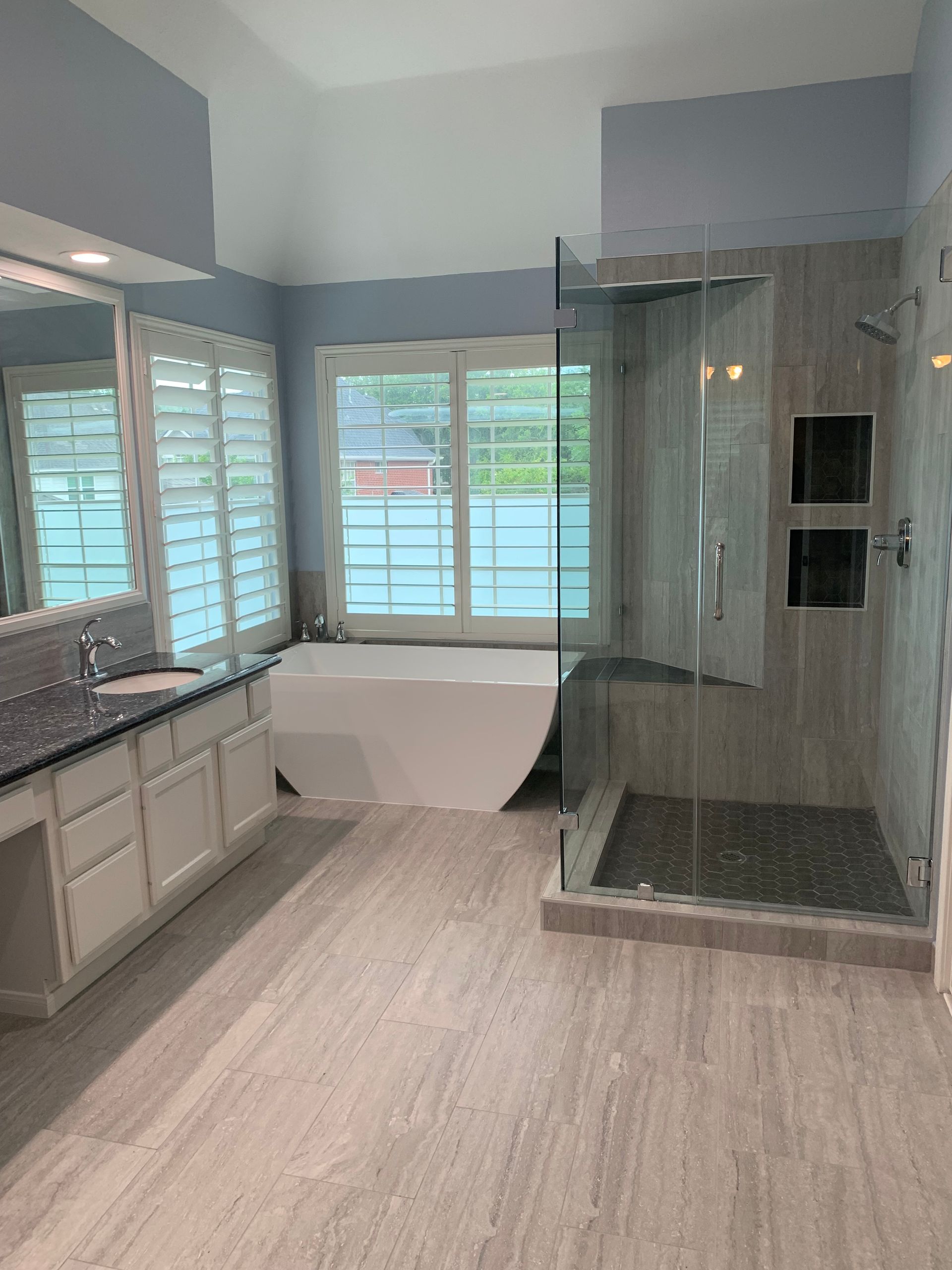 Modern bathroom with freestanding tub, glass shower, double vanity, and large windows