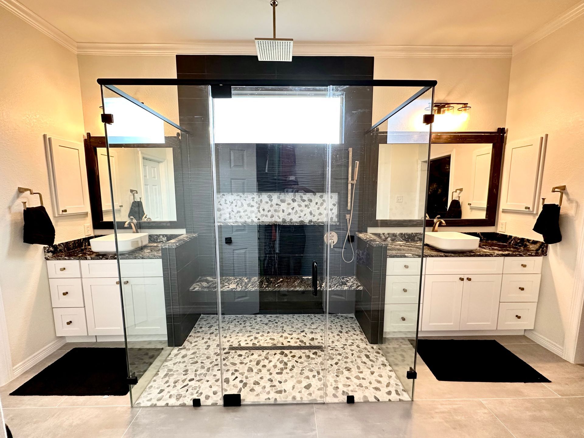Modern bathroom with double sinks, black accents, and a large central glass shower enclosure.