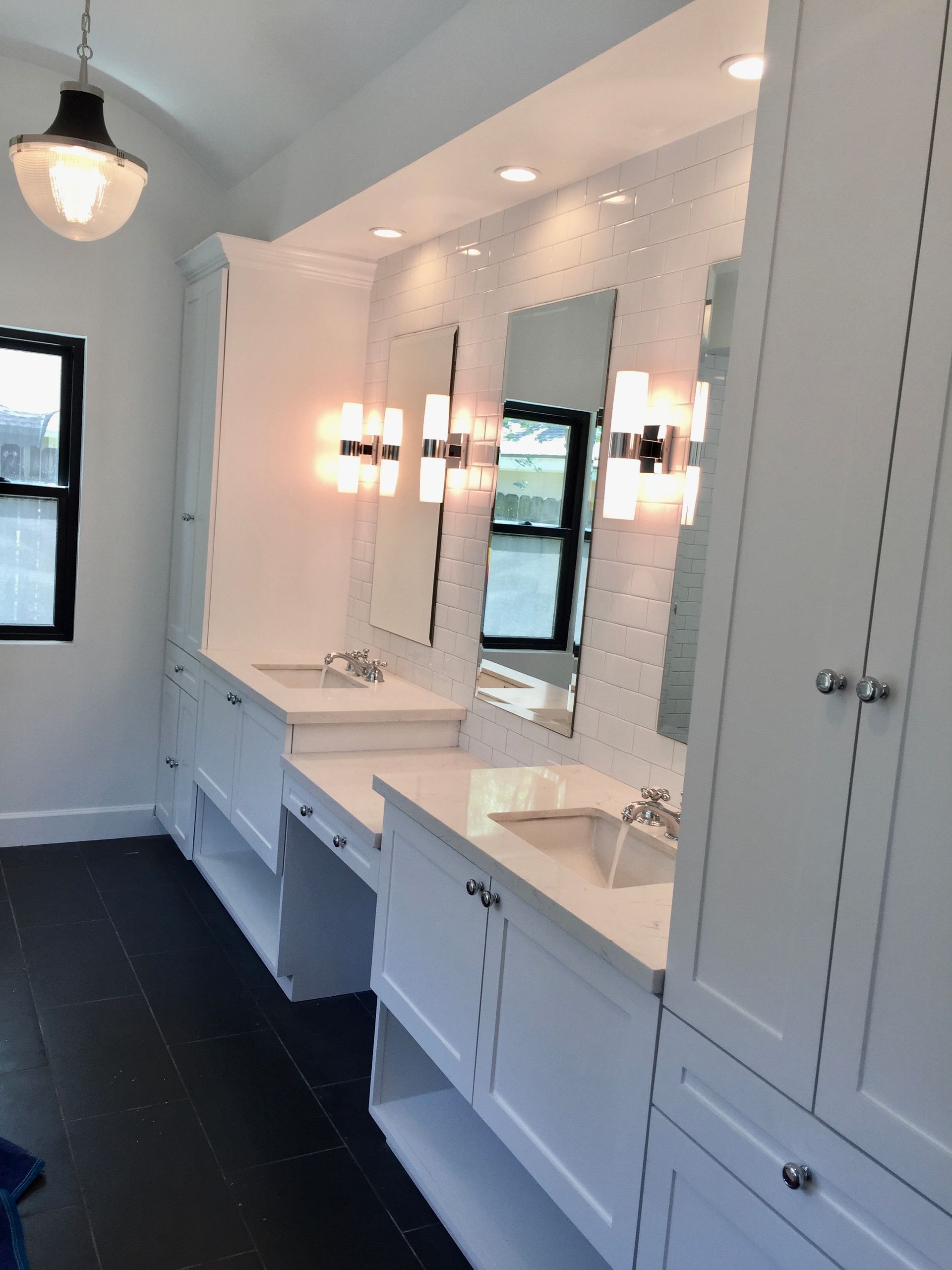 Bright white bathroom vanity with dual mirrors, sinks, and wall sconces in a modern interior.