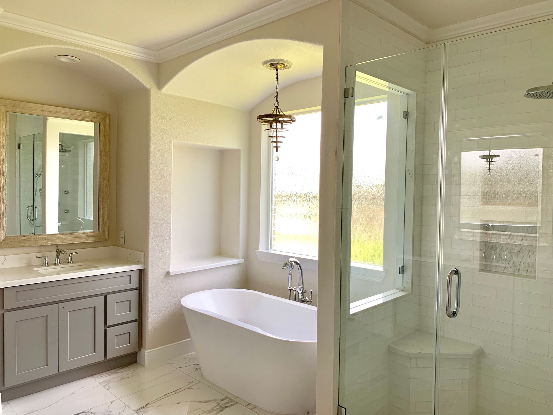 Bright beige bathroom with freestanding tub, glass shower, and vanity with mirror.