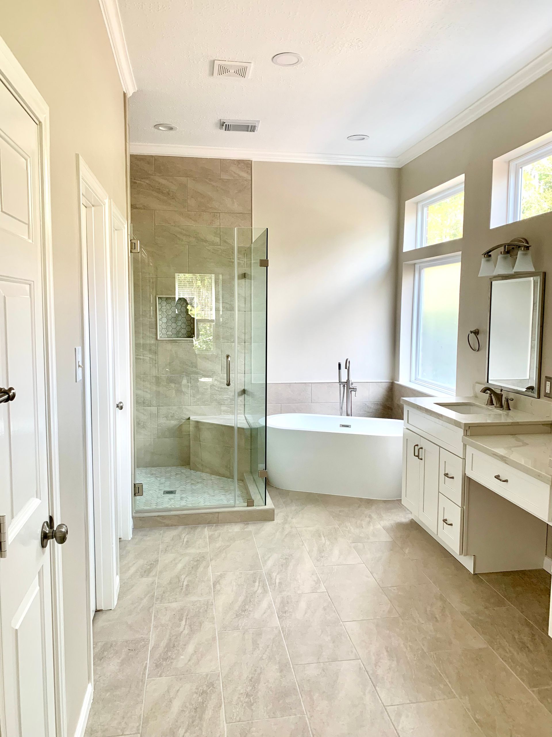 Bright bathroom with glass shower, freestanding tub, vanity, and light tile flooring