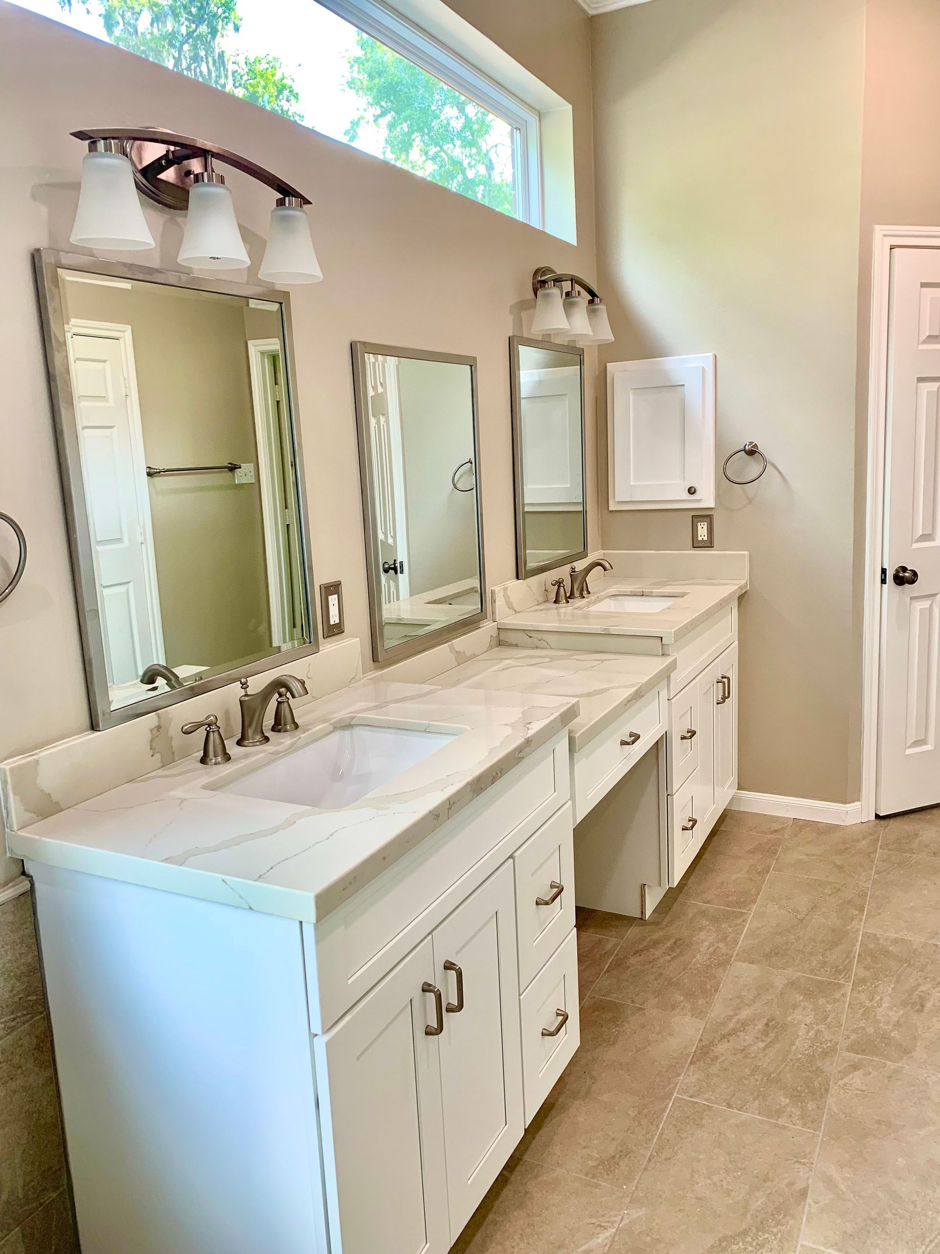 Bright bathroom with double vanity, three mirrors, white cabinets, and beige tile floor