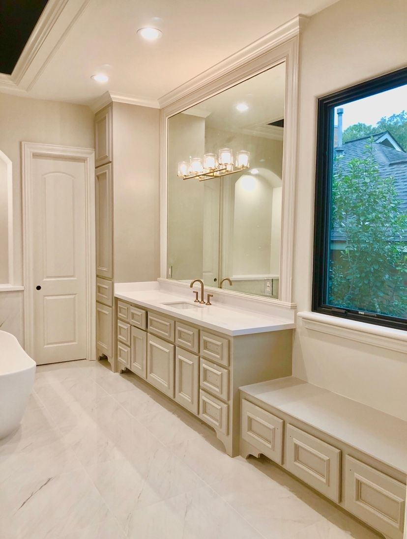 Elegant cream bathroom with double vanity, large mirror, chandelier, and window seat