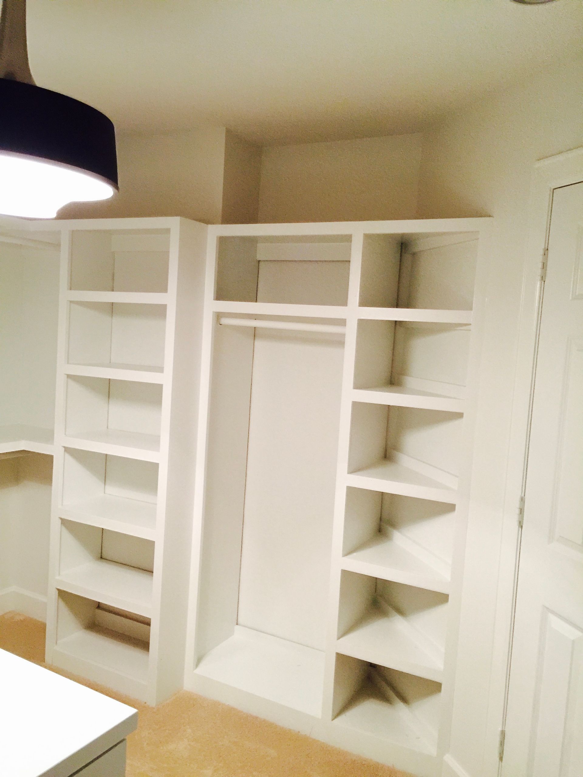 White built-in closet organizer with shelves and hanging space in a beige room.