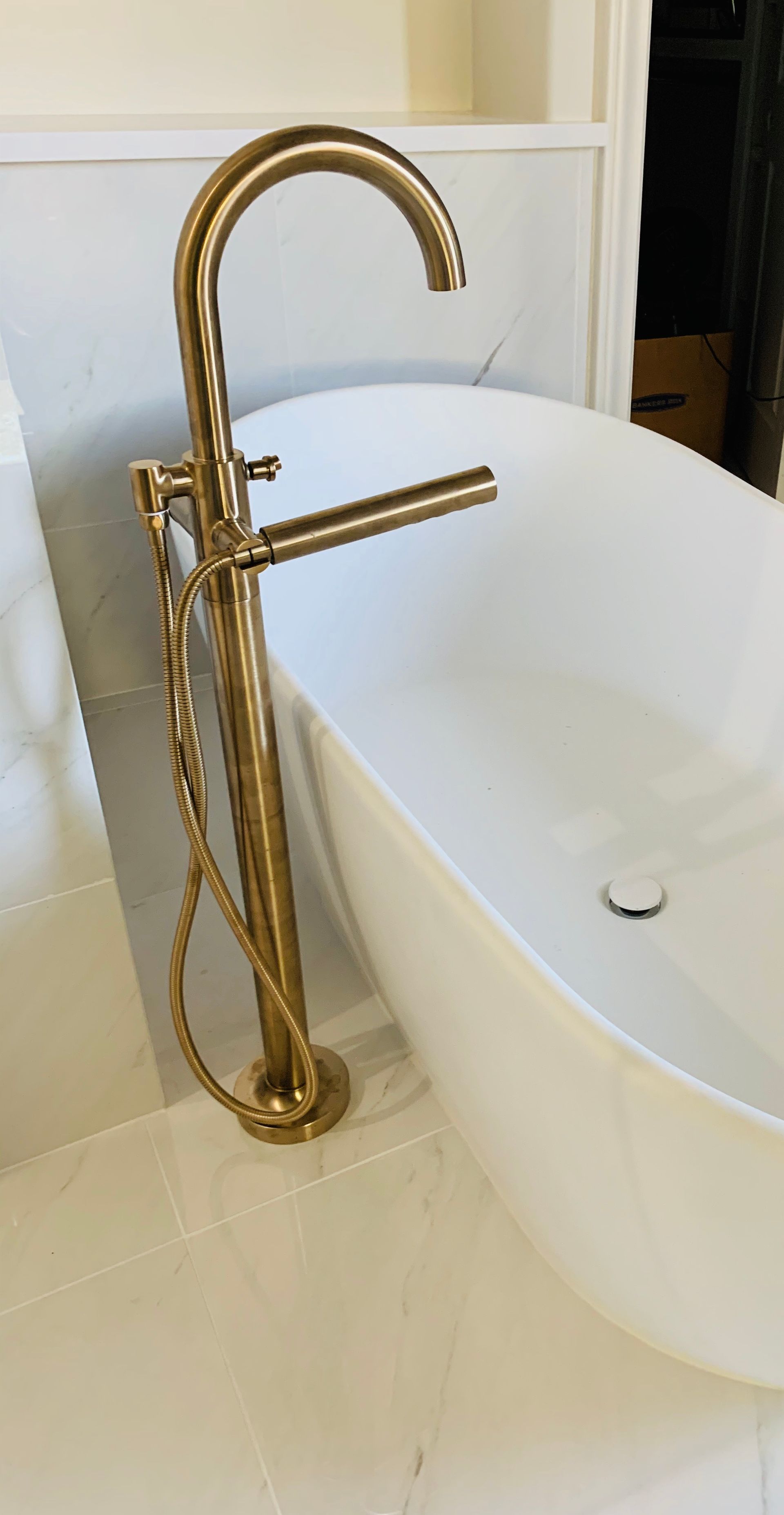 Gold freestanding bathtub faucet beside a white oval tub in a bright bathroom