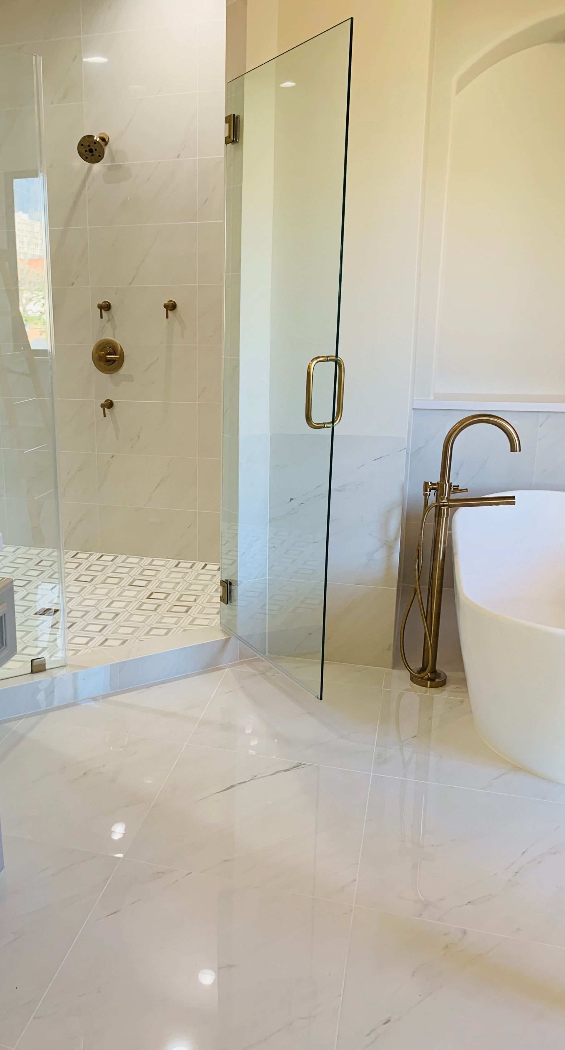Bright white marble bathroom with glass shower, bathtub, and gold fixtures